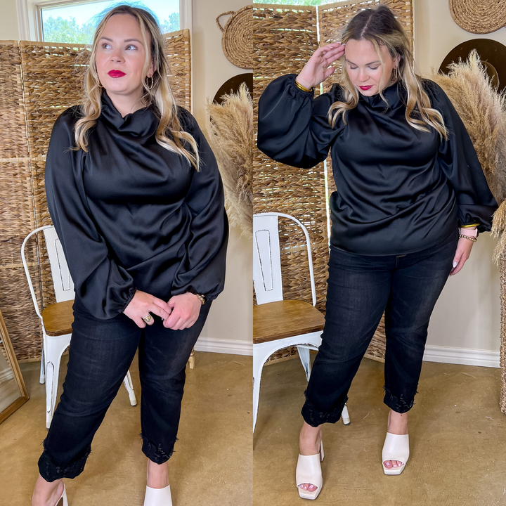 Model is wearing an black long sleeve cowl neck top. Model has it paired with black jeans, white heels, and gold jewelry.