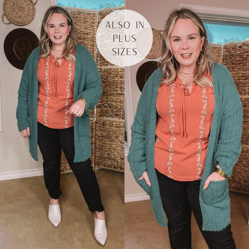 Model is wearing a clay orange shirt with a teal cardigan with pockets and has it paired with white booties and black skinny jeans. Model is wearing gold jewelry. Model is wearing size Large. 