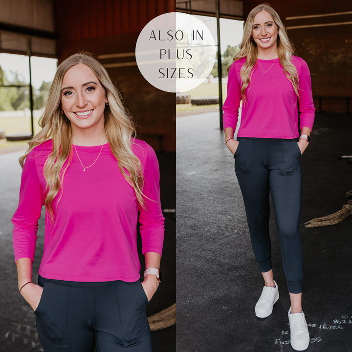 Model is wearing a hot pink long sleeve crop top. Model has it paired with black joggers, white sneakers, and gold jewelry.
