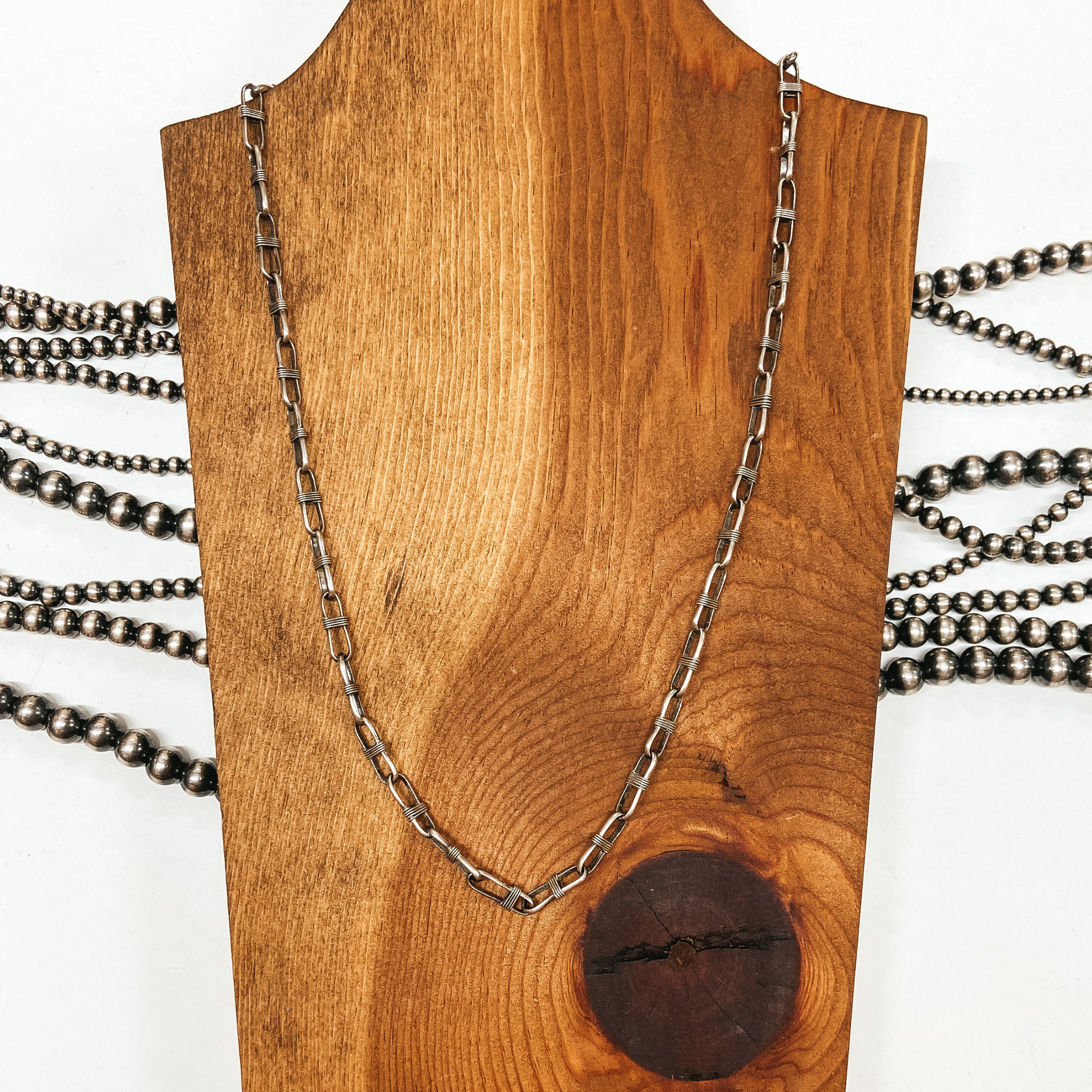 Sterling silver chain link necklace with wrapped detailing. Pictured on wooden slat with white background and Navajo pearls.