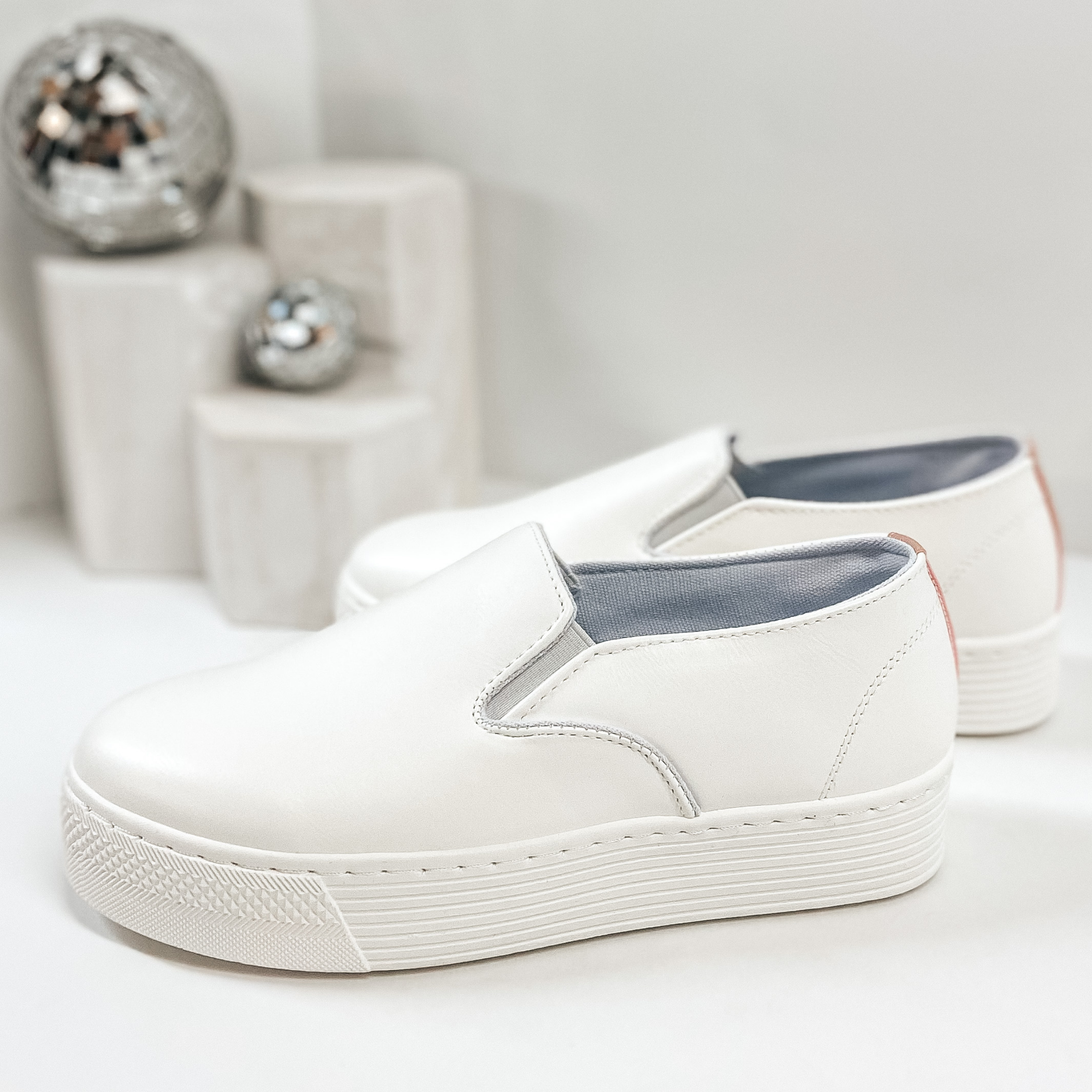 White thick sole sneakers that slip on. Pictured on white background with disco balls.