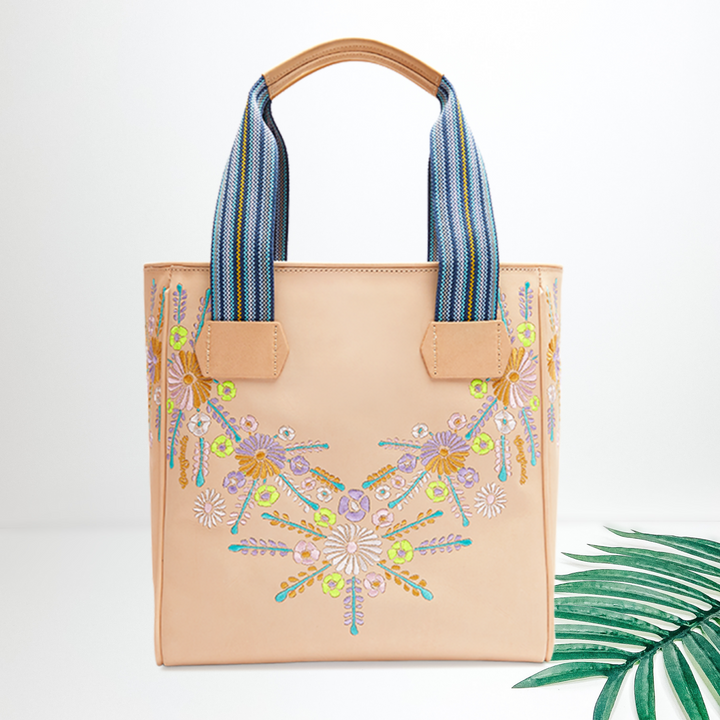A leather shoulder tote with floral embroidery. Pictured on white background with a palm leaf.