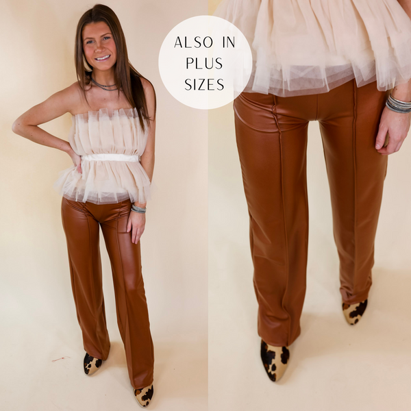 Model is wearing a pair of brown faux leather pants. Model has them paired with an ivory tulle top, cow print booties, and silver jewelry.