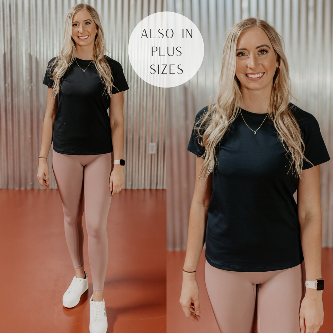 Model is wearing a black short sleeve active top. Model has it paired with dusty pink leggings, white sneakers, and gold jewelry.