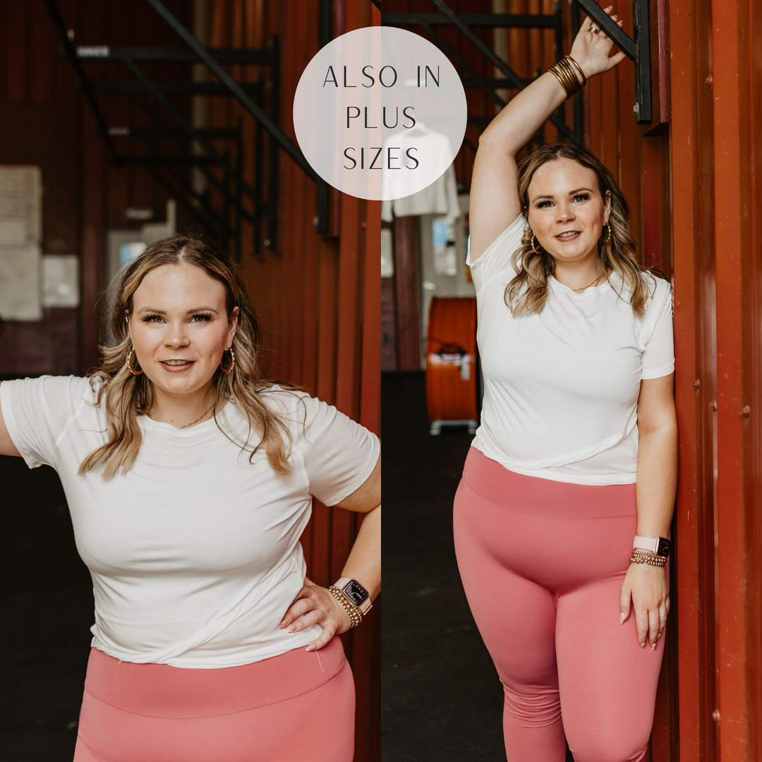 Model is wearing a white crop top with a criss cross hemline. Model has it paired with mauve leggings and gold jewelry.