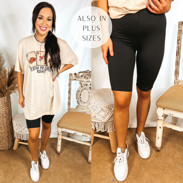 Model is wearing a pair of black biker shorts that are knee length. Model has it paired with white sneakers, an oversized tee shirt, and silver jewelry.