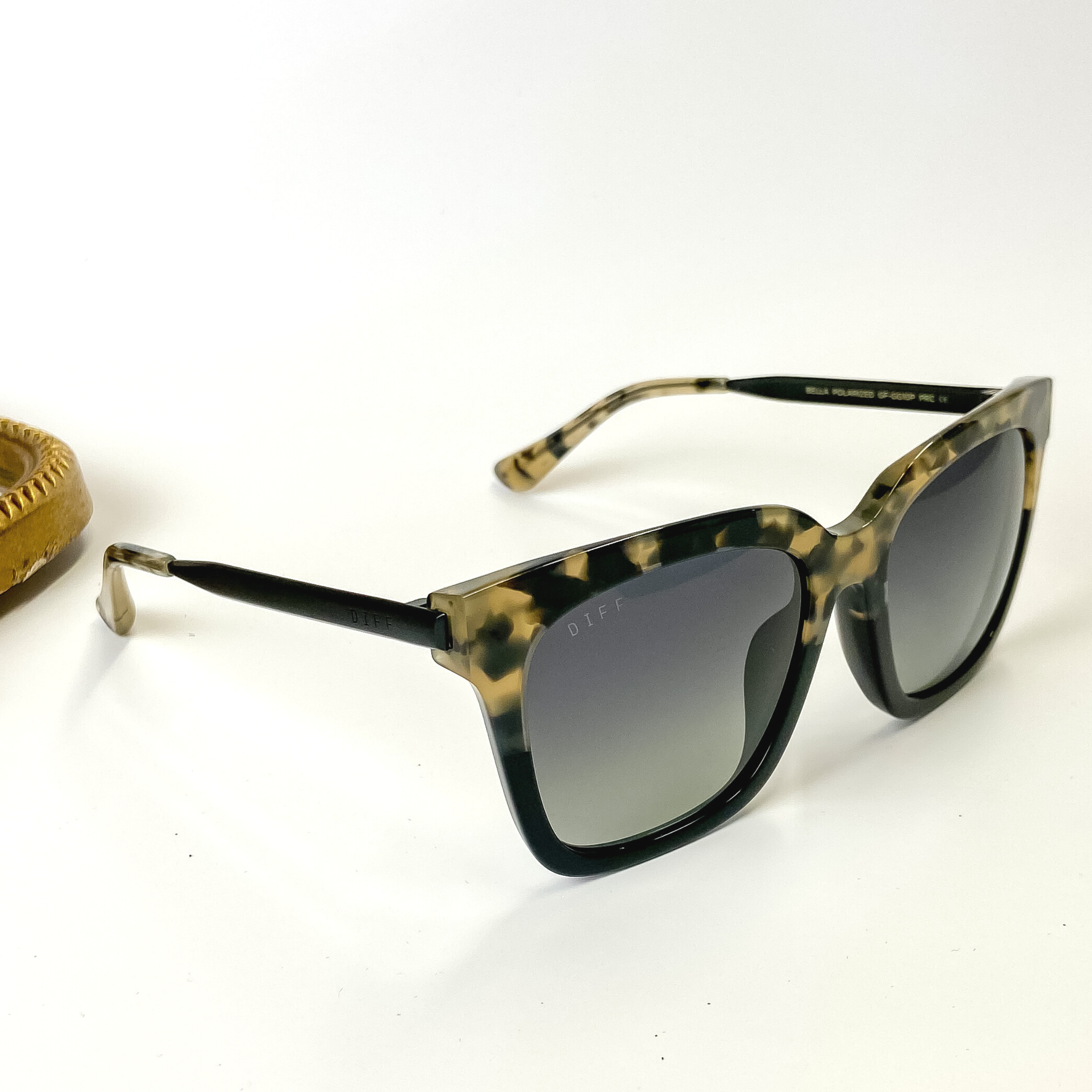 A pair of tortoise print and black frame sunglasses with grey gradient lenses. These sunglasses are pictured on a white background with gold jewelry.