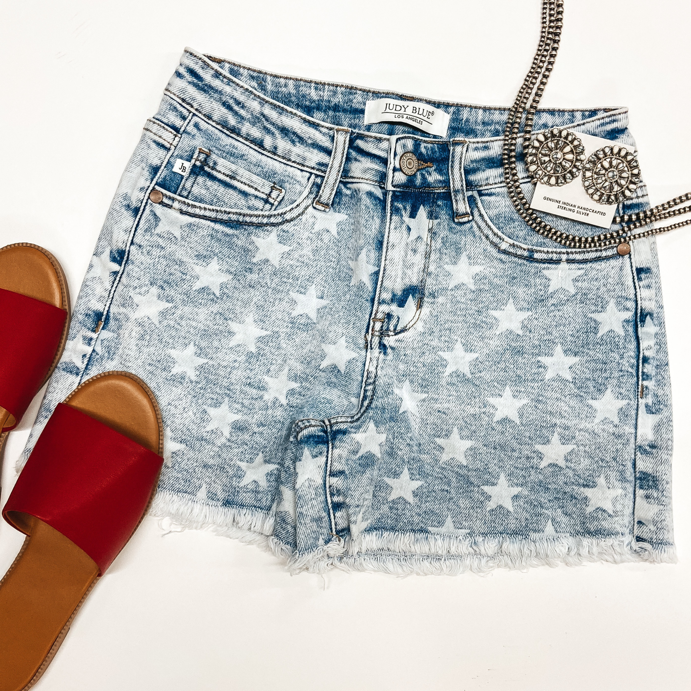 A pair of star print cut off shorts that are light wash. These shorts are pictured on a white background with sterling silver Navajo jewelry.