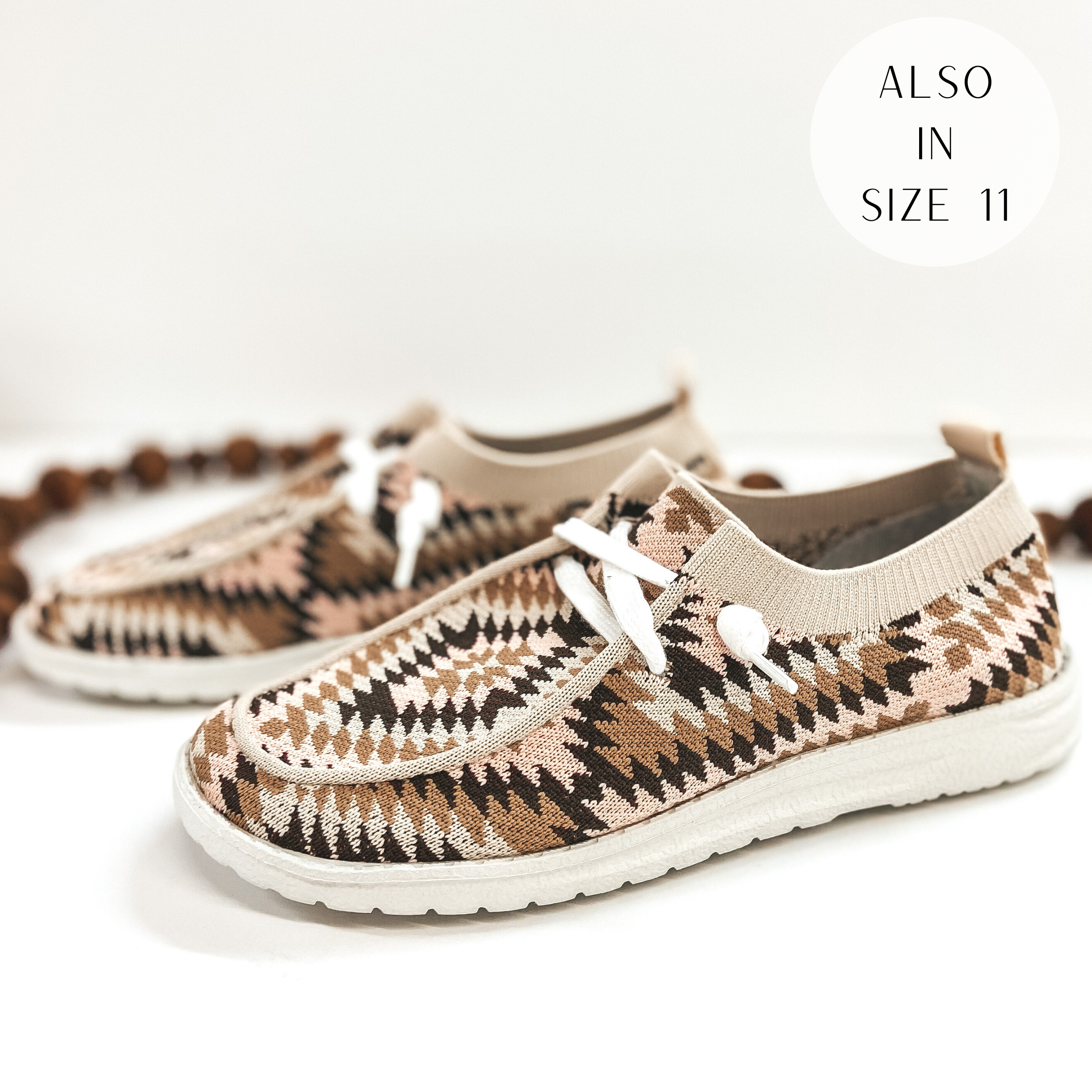 A pair of aztec print slip on loafers that are blush pink and brown. Pictured on white background with brown beads.