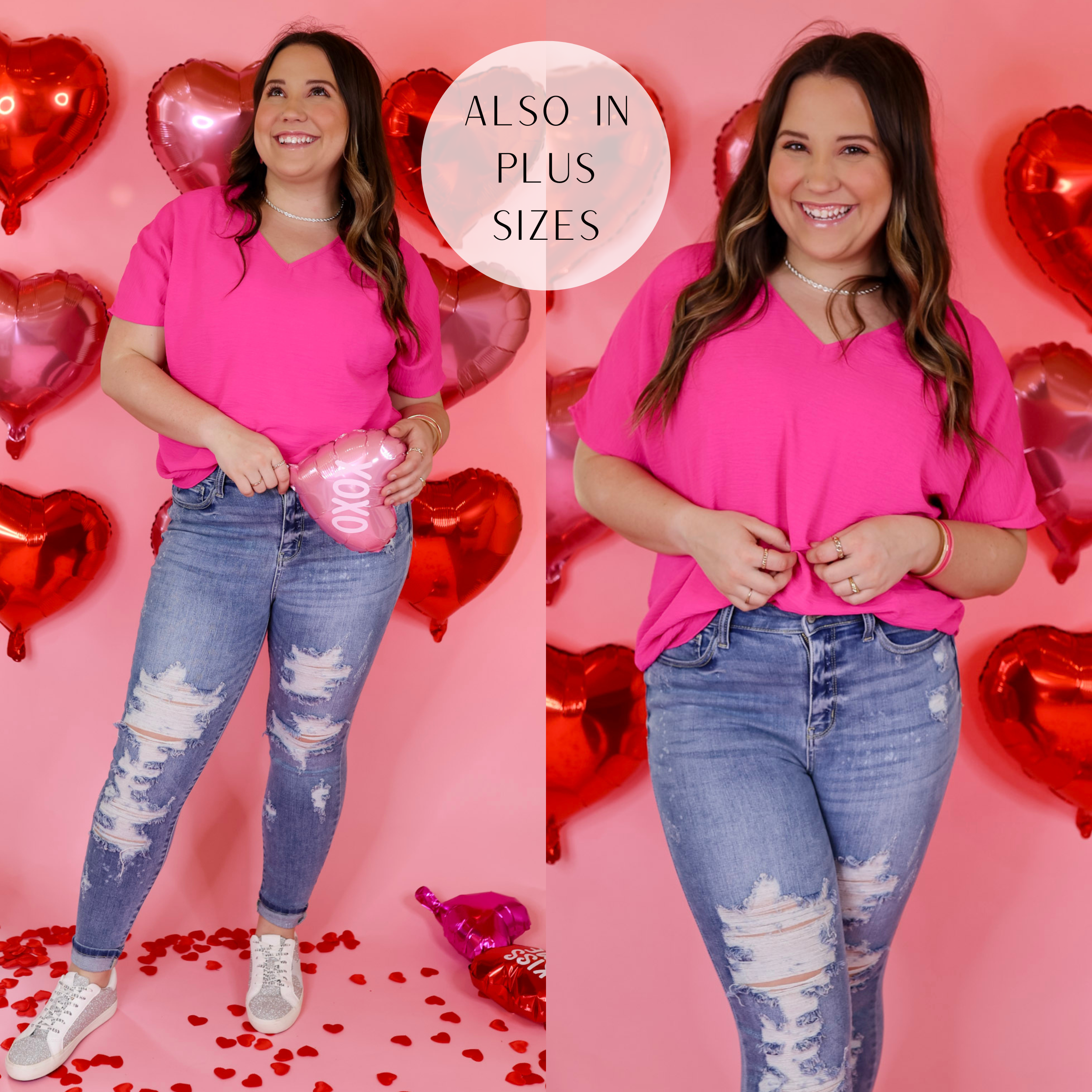 Model is wearing a short sleeve, v neck, top in fuchsia pink. Model has this top paired with jeans, silver sneakers, and silver jewelry. Background is solid pink with red heart balloons. 