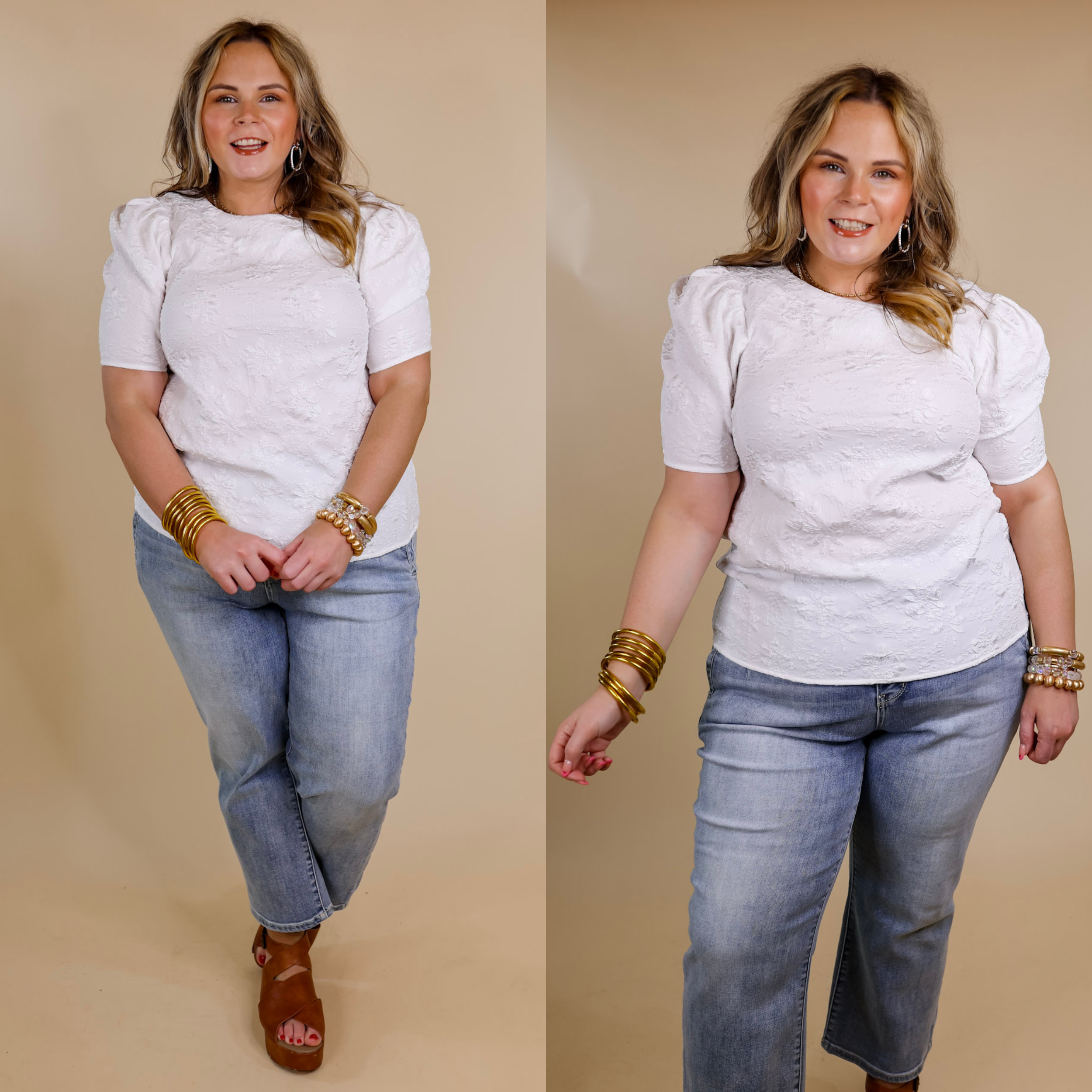 Model is wearing a floral embossed top with short puff sleeves in white. Model has it paired with light wash jeans, tan sandals, and gold jewelry.