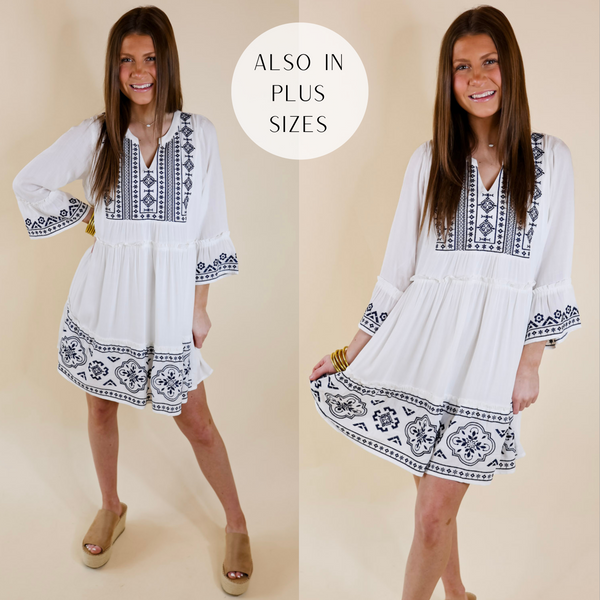 Model is wearing a white dress with navy embroidery, 3/4 sleeves, and a notched neckline. Model has this dress paired with tan wedges and gold jewelry.