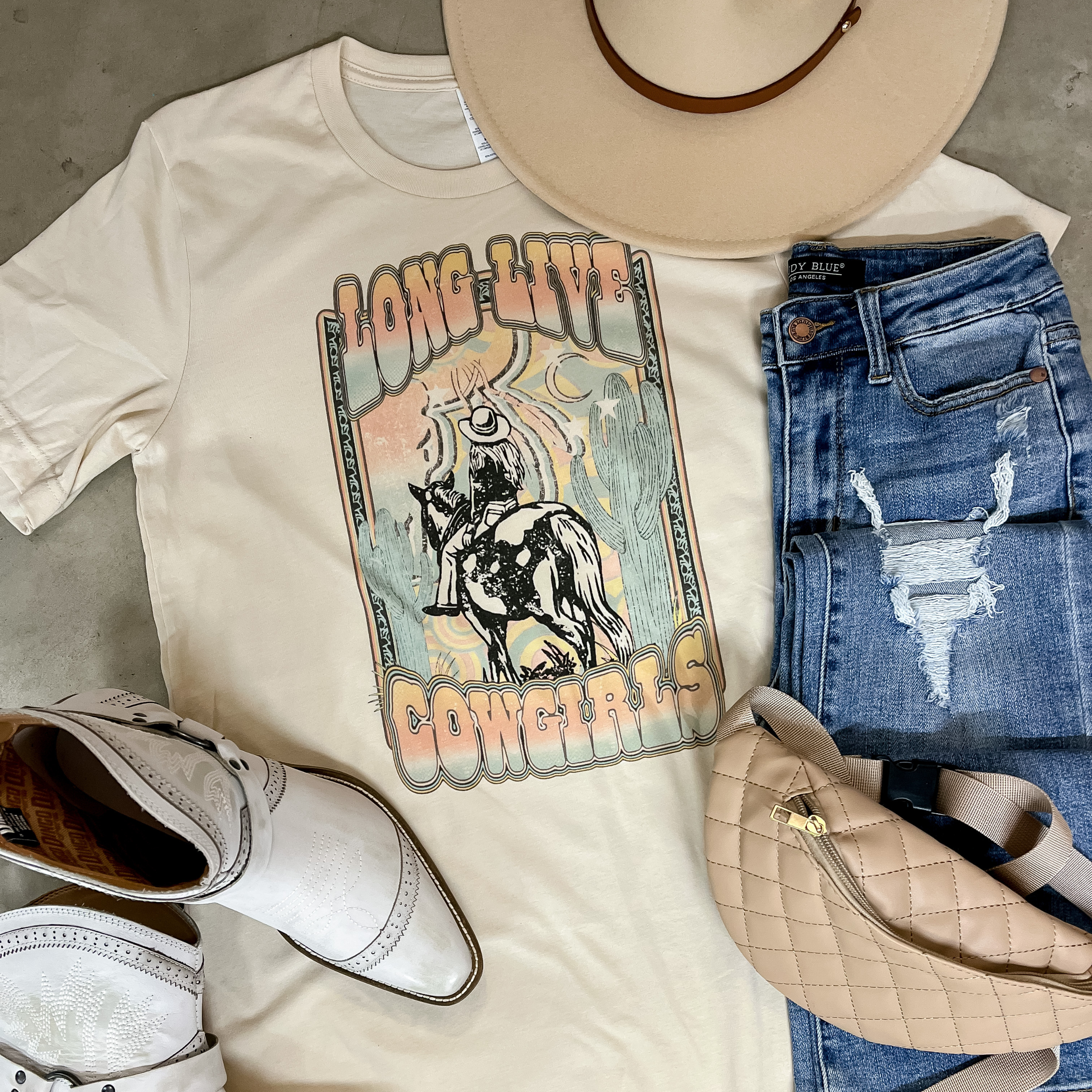 this graphic tee in cream includes a cute cowgirl design that reads "long live cowgirls" in a multi color. This tee is paired with medium wash, distress blue jeans, white booties, a cream hat, and a cream fanny pack. 