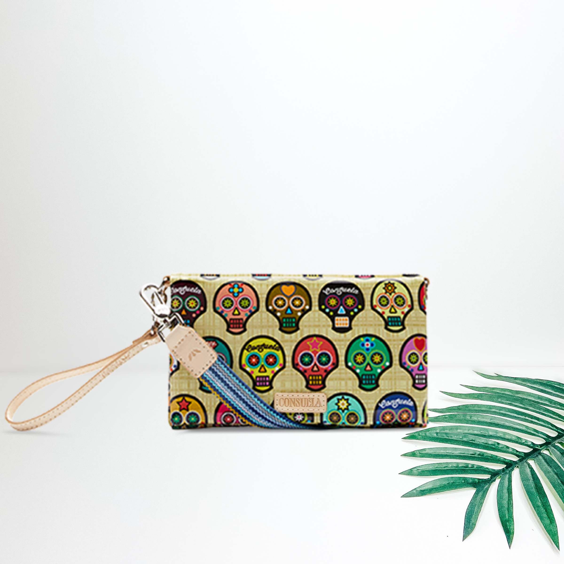 A sugar skull multi color wallet with a cross body strap. Pictured on white background with a palm leaf
