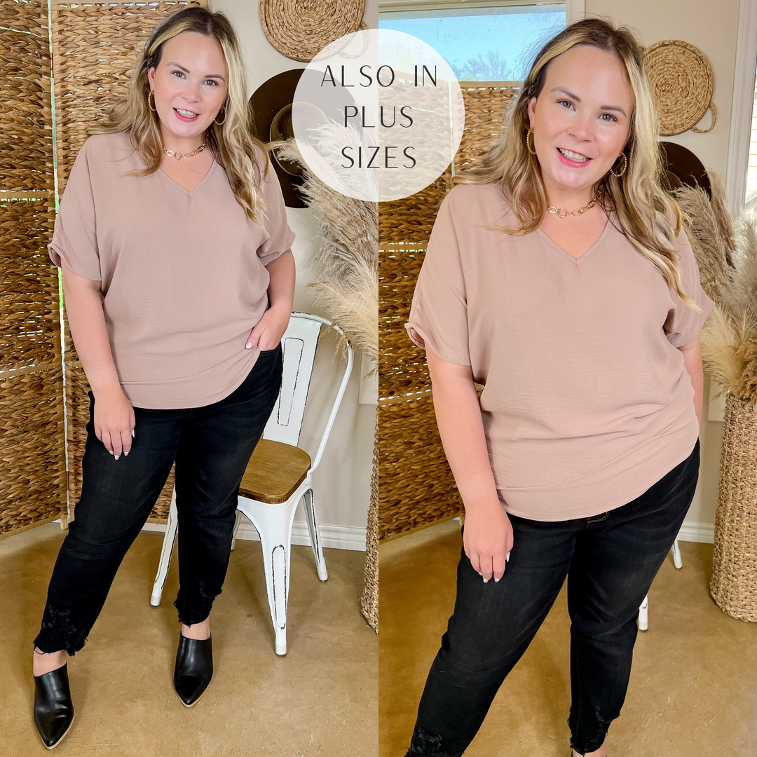 Model is wearing a taupe v neck short sleeve top. Model has it paired with black jeans, black mules, and gold jewelry.