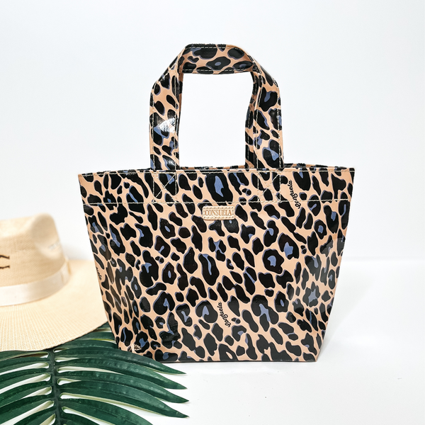 A small size leopard print bag with handles. Pictured on white background with palm leaf and straw hat.