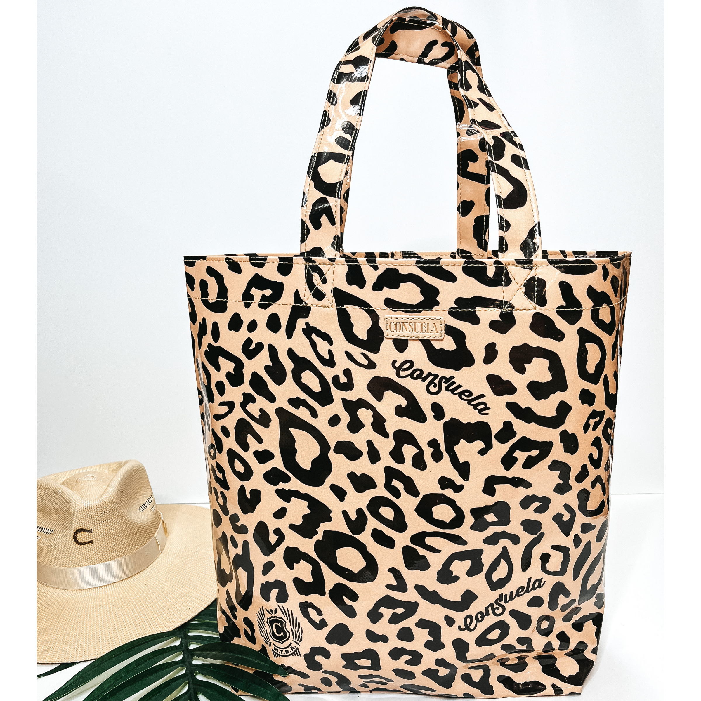 A large size leopard print bag with handles. Pictured on white background with palm leaf and straw hat.