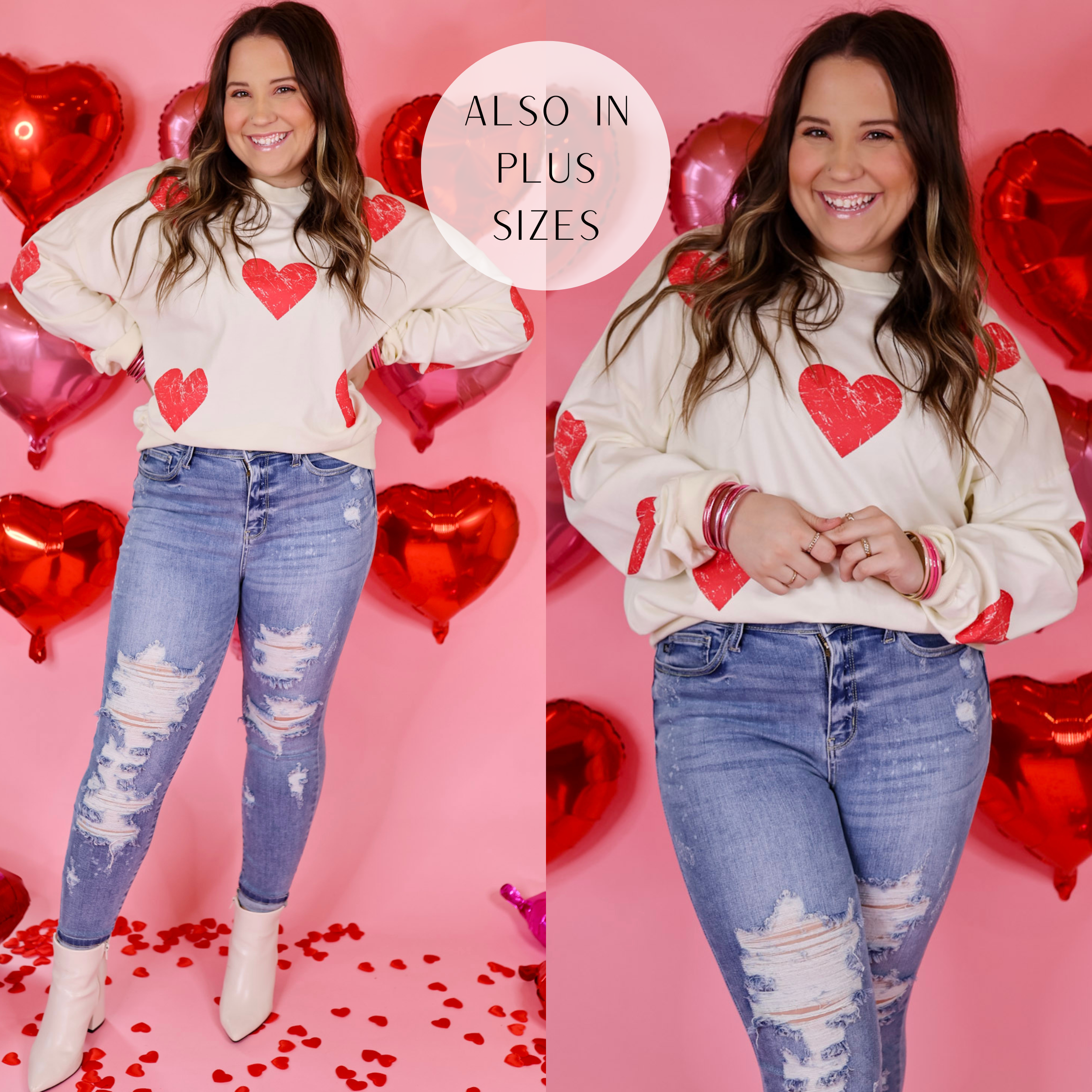 Model is wearing a white sweater with red hearts. Model has this sweater paired with skinny jeans, white booties, and gold jewelry. Background is a light pink with red balloon hearts. 