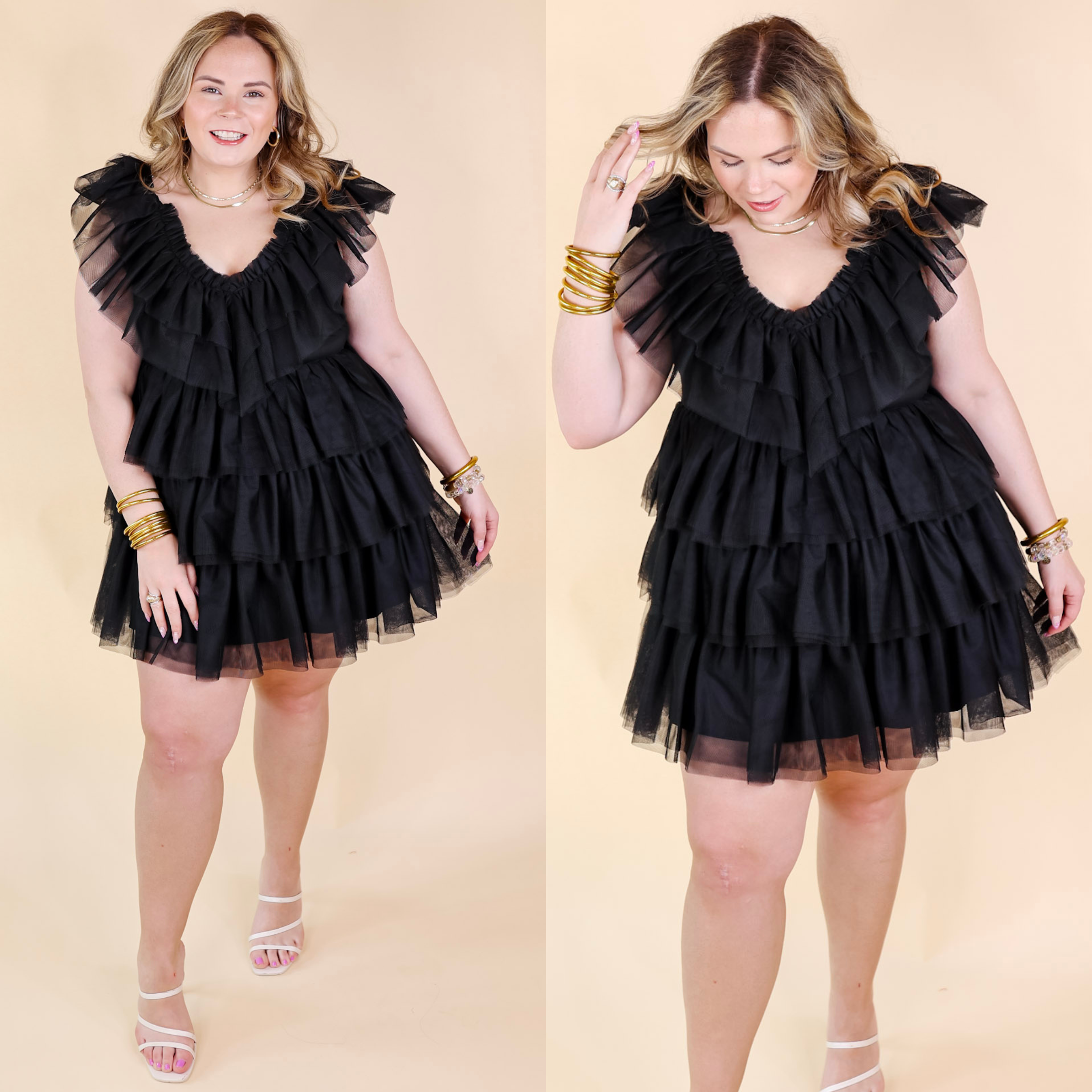 Model is wearing a black short dress made of ruffle tulle. Model has this dress paired with white strappy heels and gold jewelry.