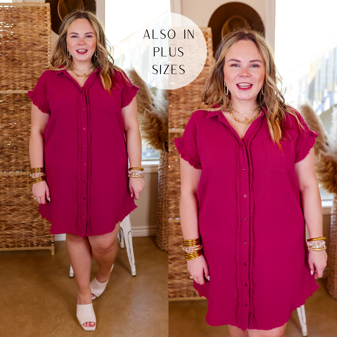 Model is wearing a knee length, button down, raspberry red dress with a raw hem. Model has this dress paired with white heels and gold jewelry.  