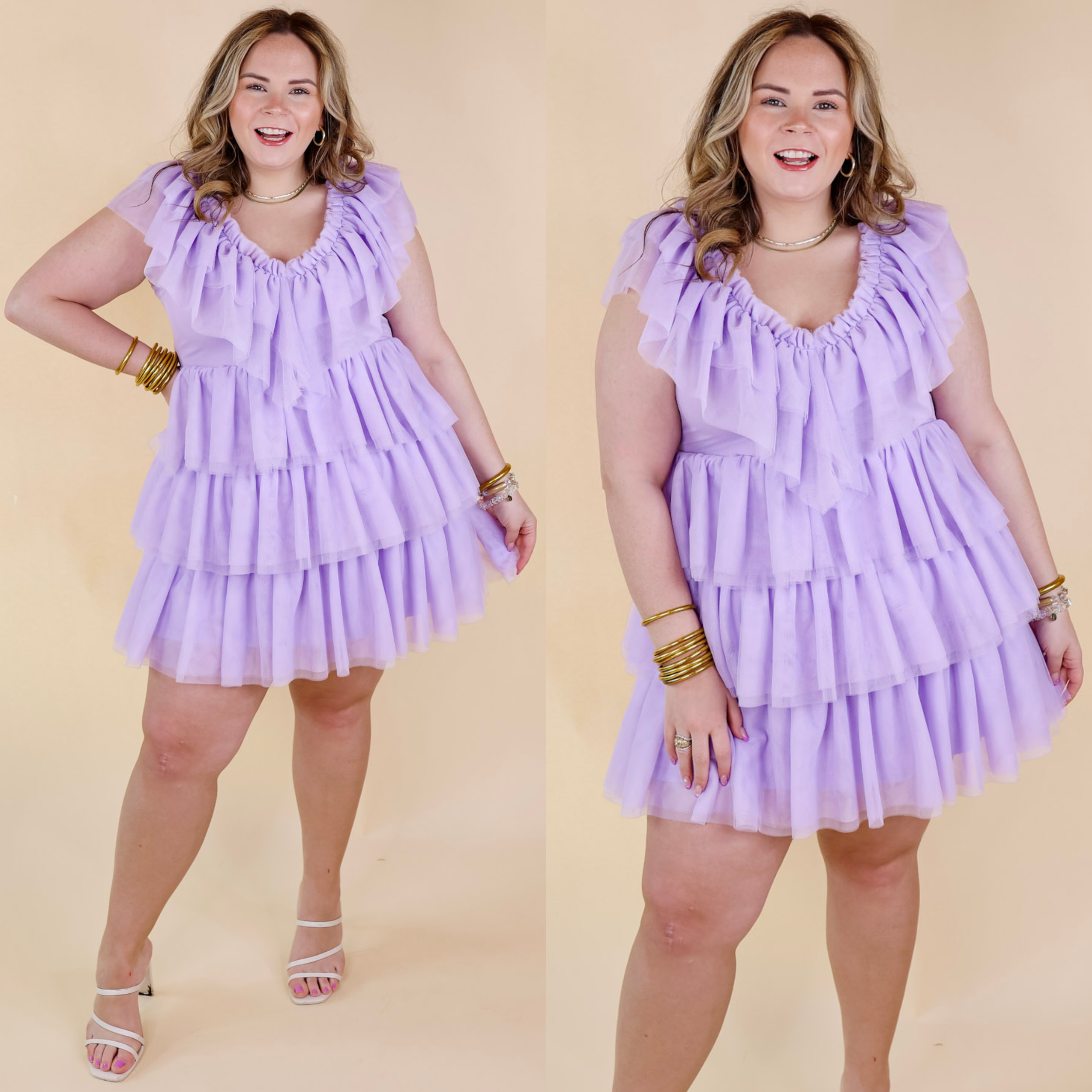Model is wearing a lavender purple short dress made of ruffle tulle. Model has this dress paired with white strappy heels and gold jewelry.