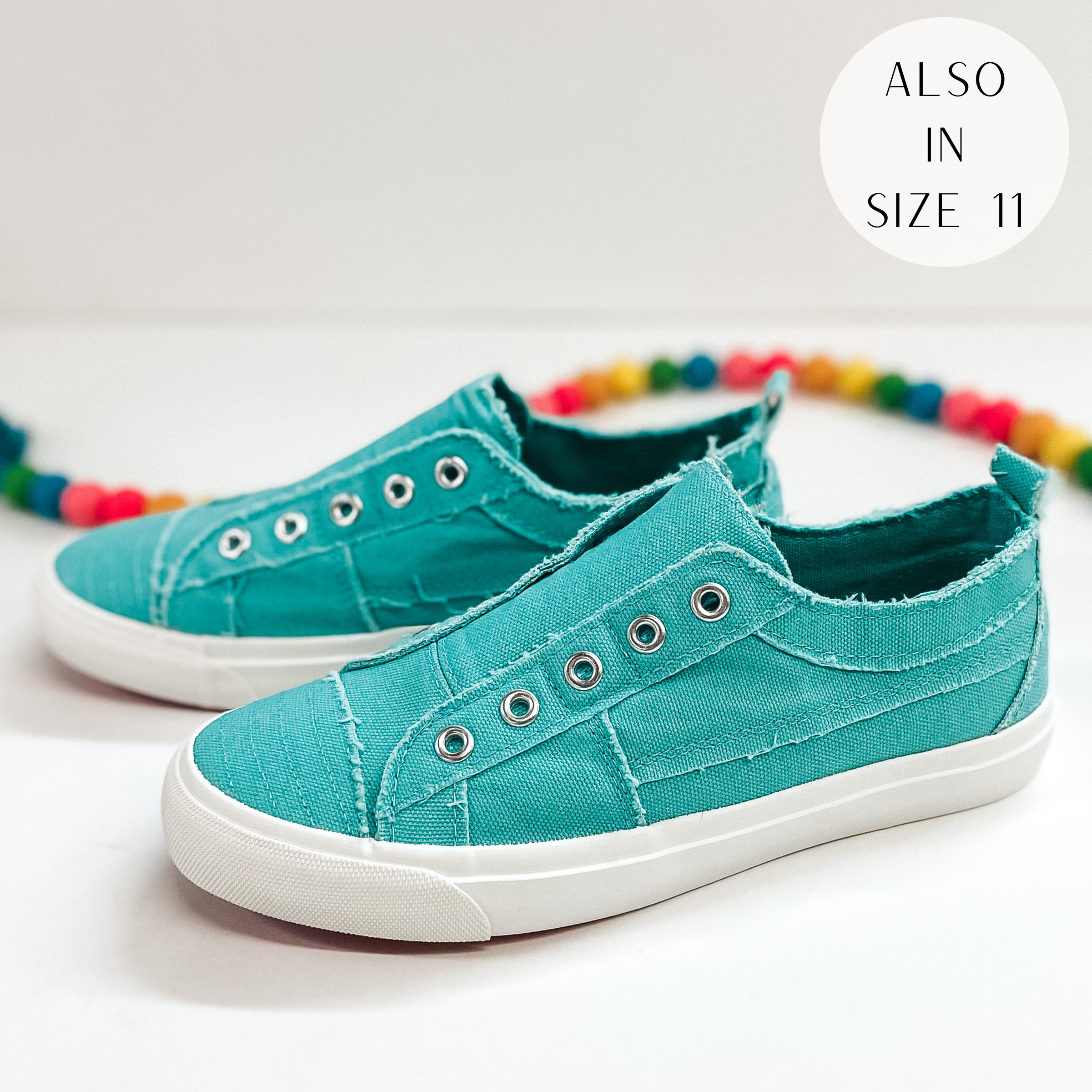 A pair of aqua blue sneakers that do not have laces. Pictured on white background with colorful beads.