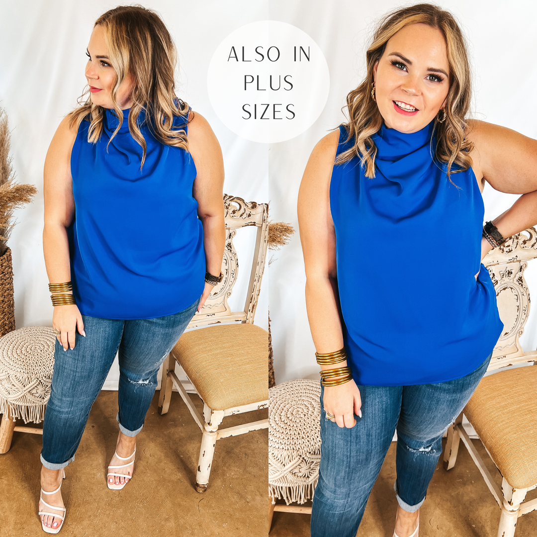 Model is wearing a blue tank top with a high cowl neck. Model has it paired with distressed skinny jeans, strappy sandals, and gold jewelry.