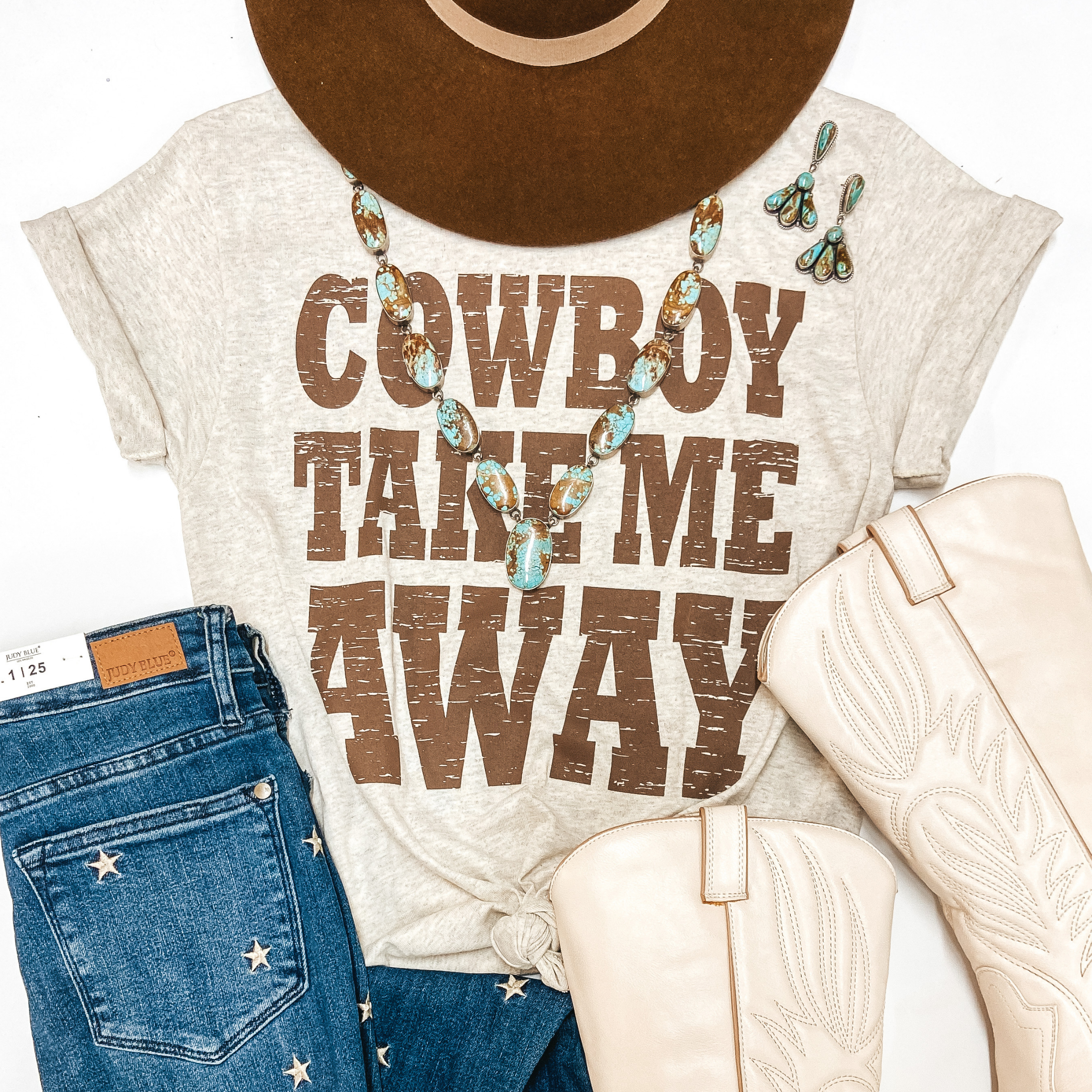 A heather beige graphic tee that has cuffed sleeves and a knotted front. The tee shirt says "Cowboy Take Me Away" in brown writing. The tee shirt is pictured on white background with genuine turquoise jewelry, star print jeans, ivory cowgirl boots, and a brown hat.