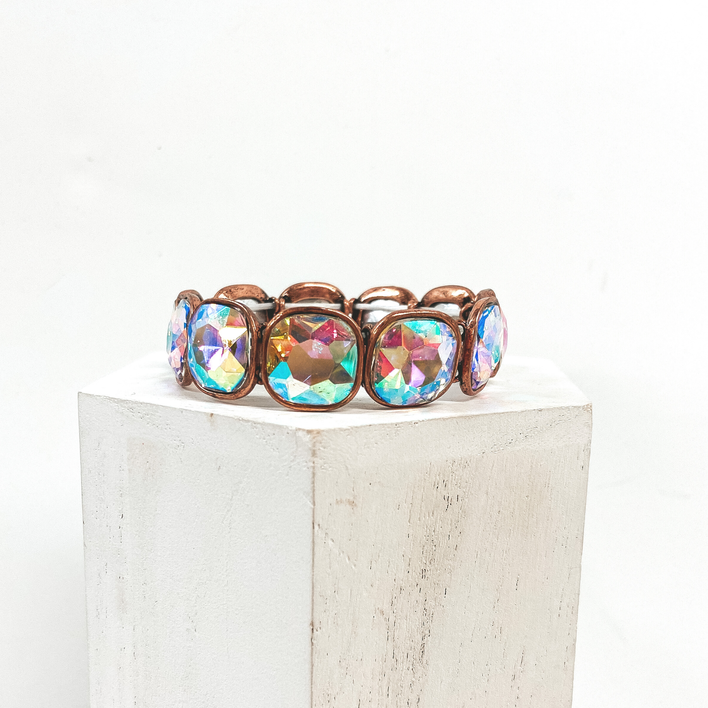 A square crystal bracelet with a copper outline. Placed on white column against white background.