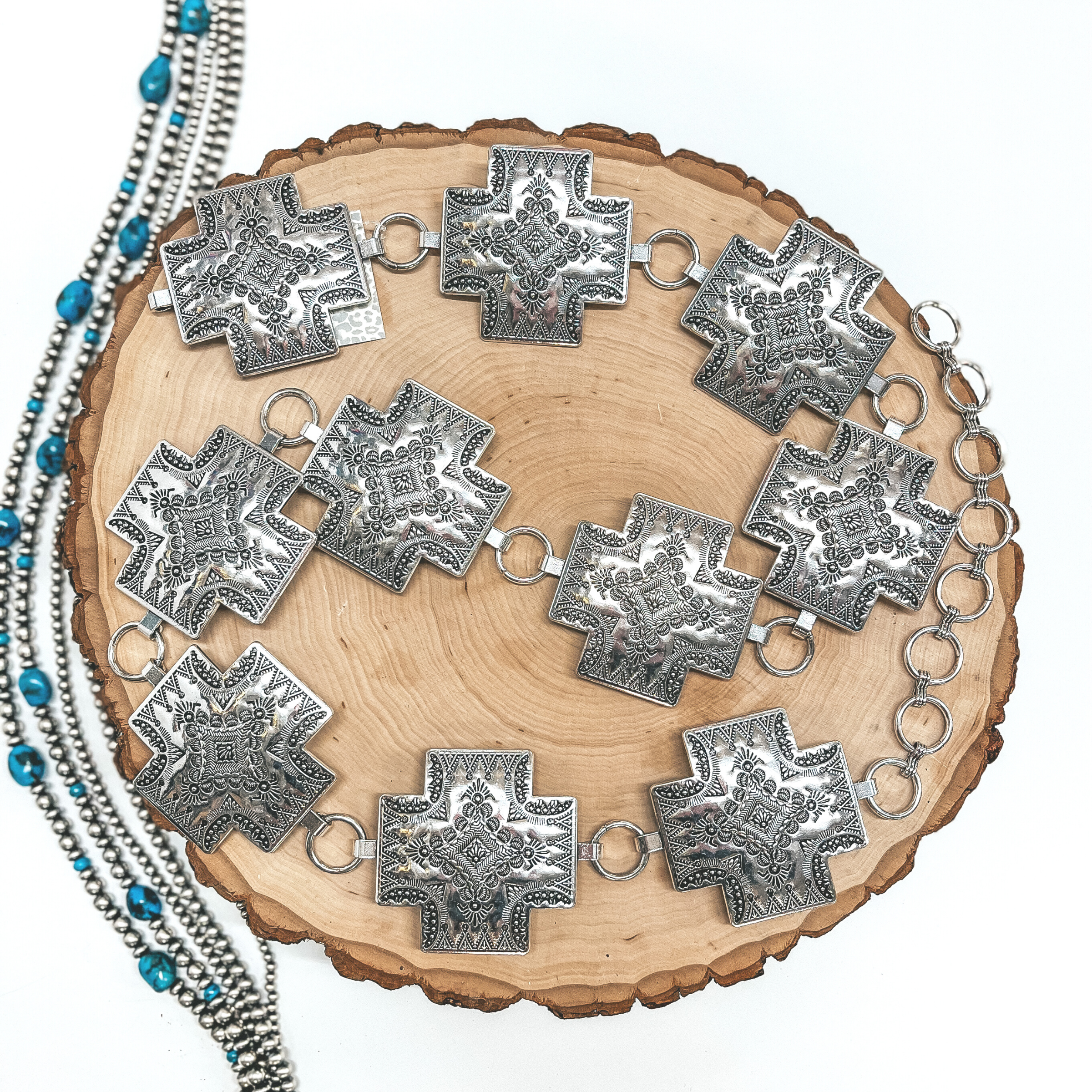 A silver cross concho belt pictured on a wooden display on white background with Navajo pearls