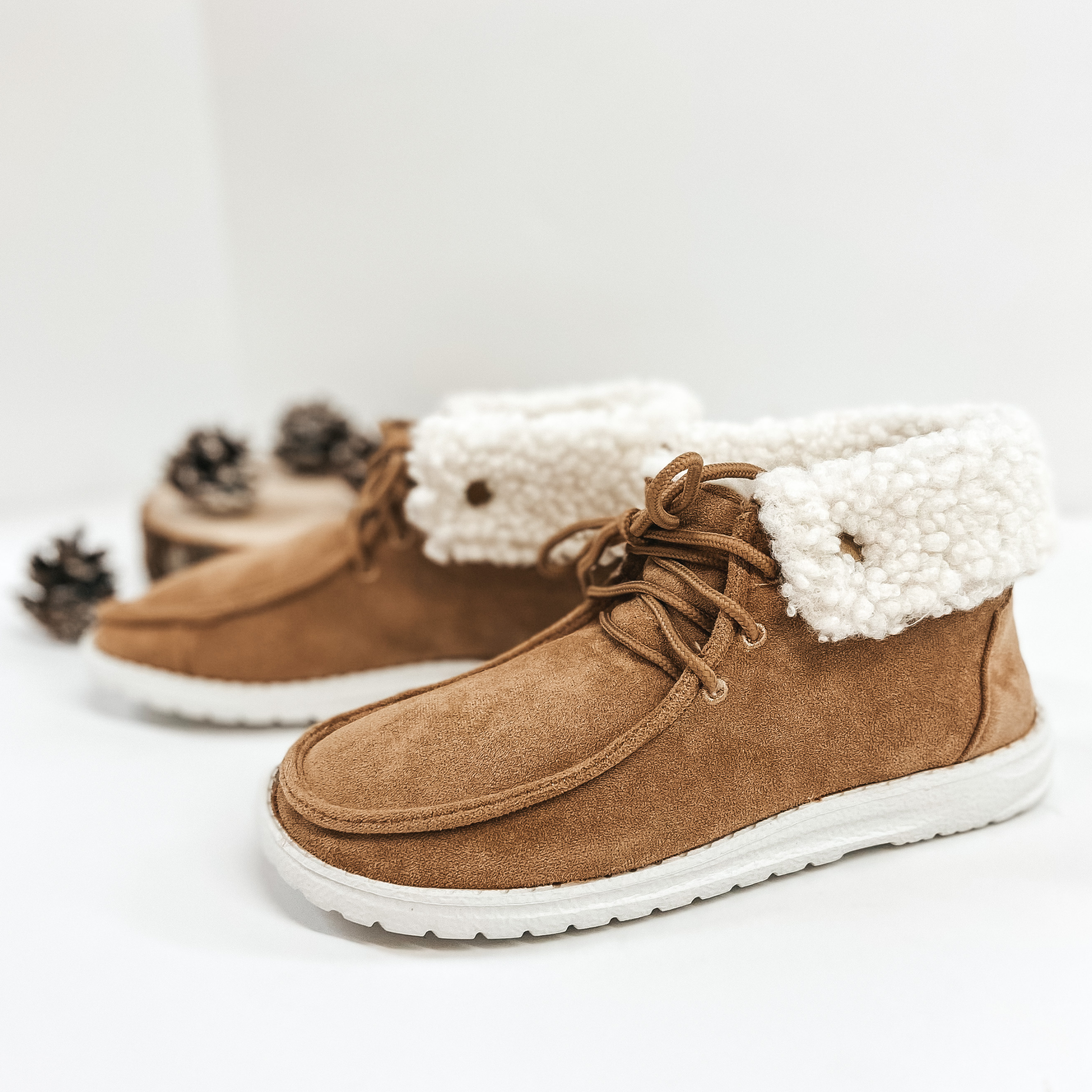 Fleace lined high top sneakers that are a soft tan. Pictured on white backgroynd with pinecones.