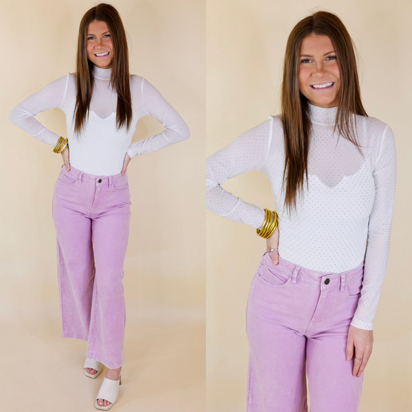 Model is wearing a white long sleeve bodysuit with crystals. Model has it paired with purple jeans, ivory heels, and gold jewelry.