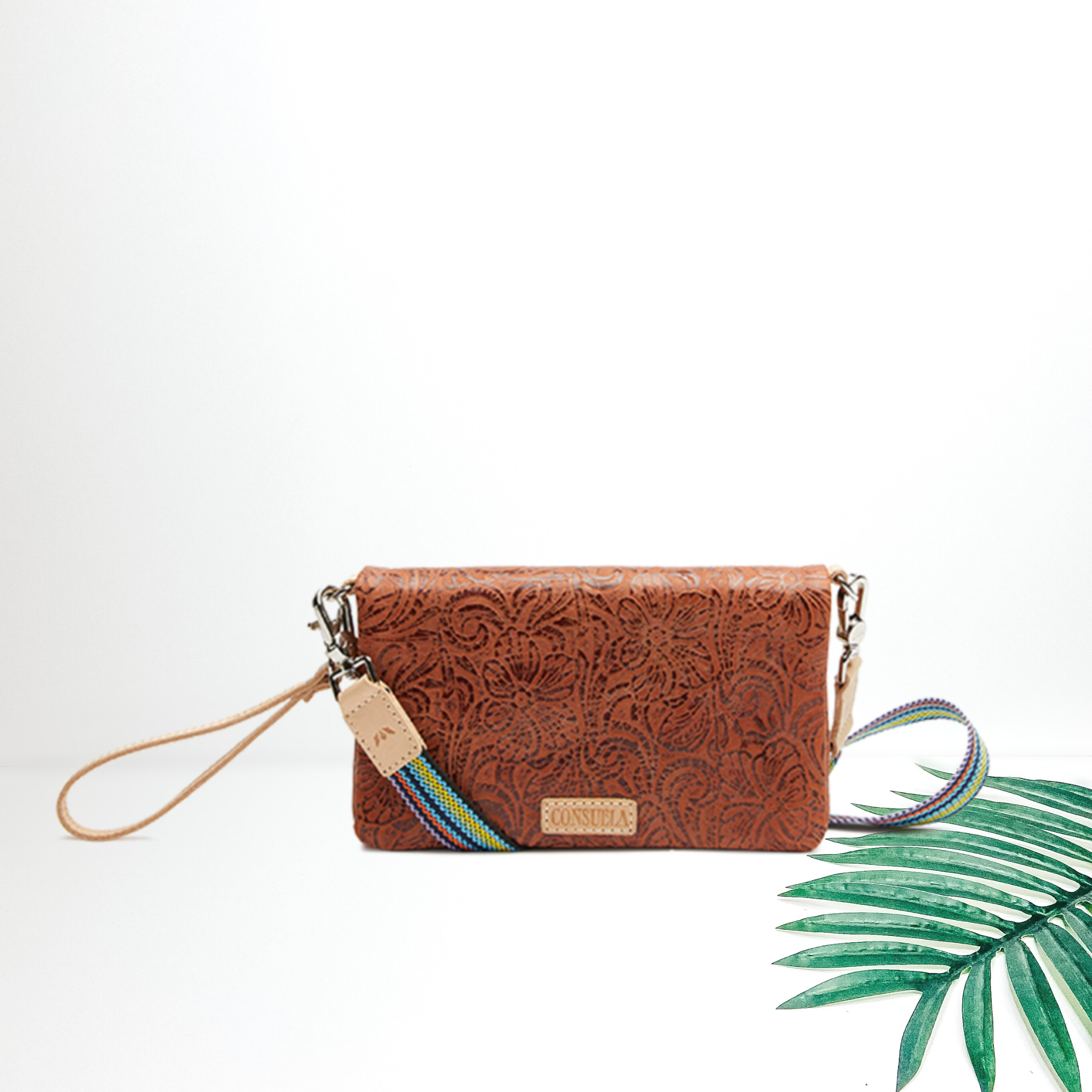 A tooled leather pattern crossbody purse pictured on a white background with a palm leaf.