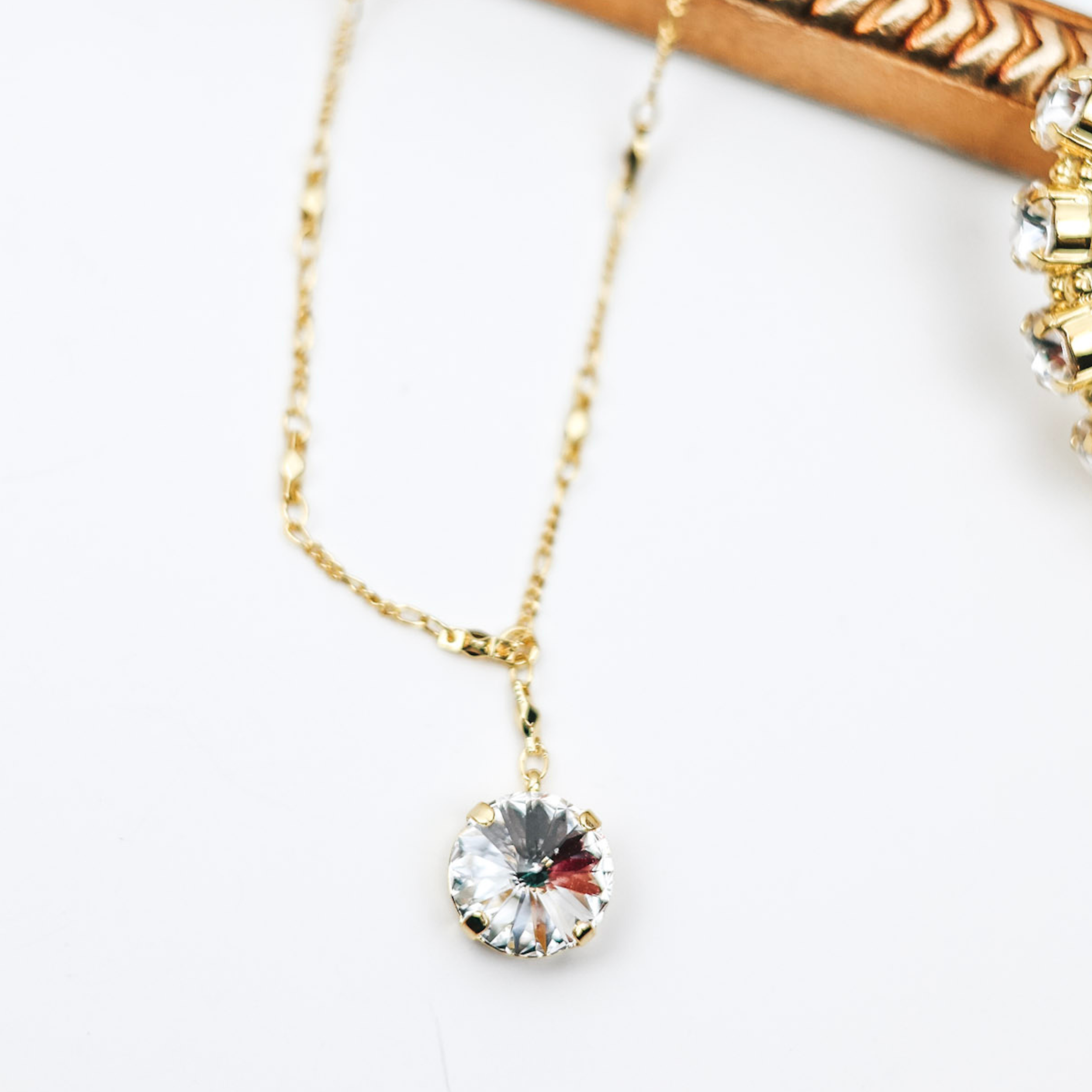 A gold tone necklace with a chain drop with a large circle crystal attached. Pictured on a white background.