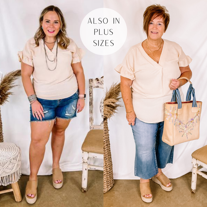 Model is wearing a beige ruffle short sleeve top. Model has it paired with distressed denim shorts, tan wedges, and silver jewelry.