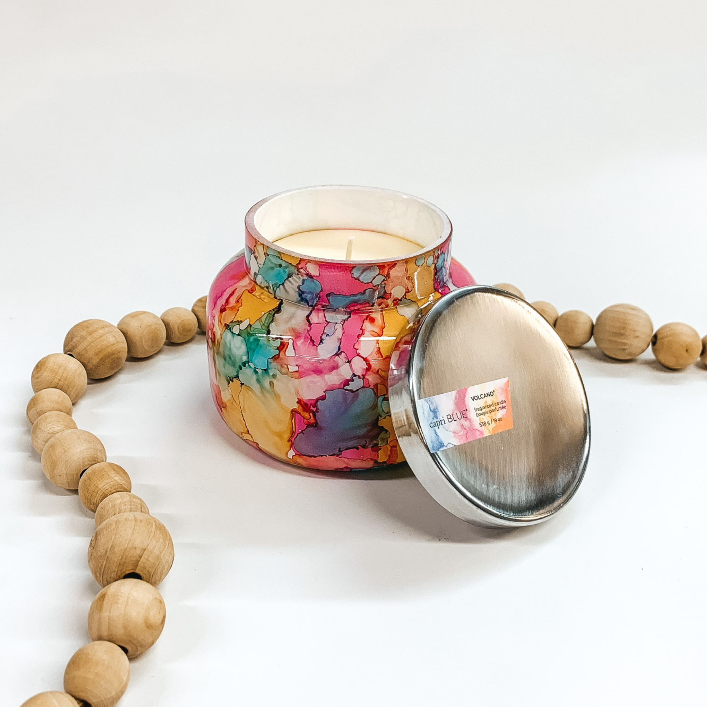 A rainbow watercolor glass jar candle with metal lid. Pictured on white background with wooden beads.