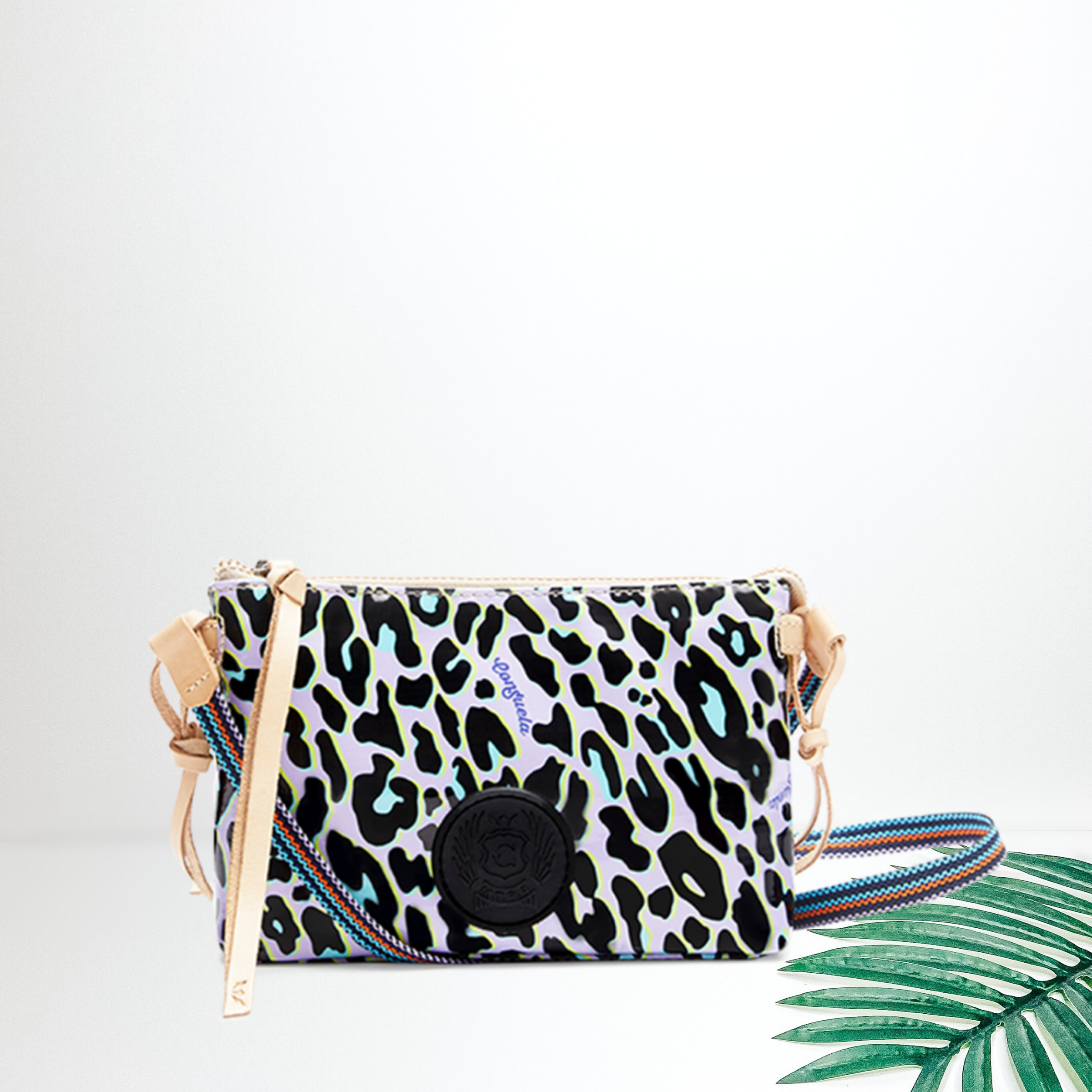 A purple leopard print crossbody bag pictured on white background with a palm leaf.