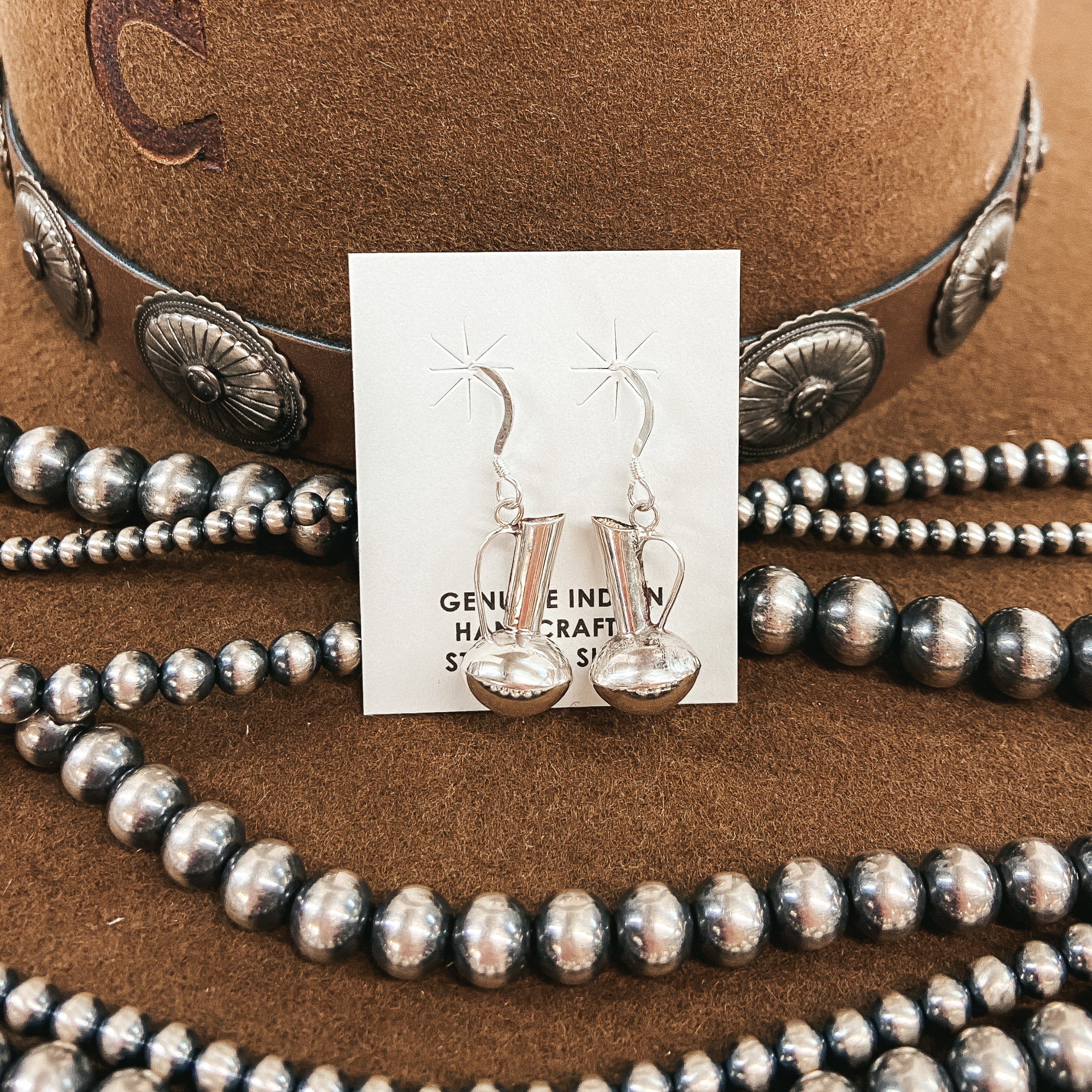 Sterling silver pitcher shaped earrings on sterling silver fishhook. Pictured on a brown felt hat with Navajo pearls.