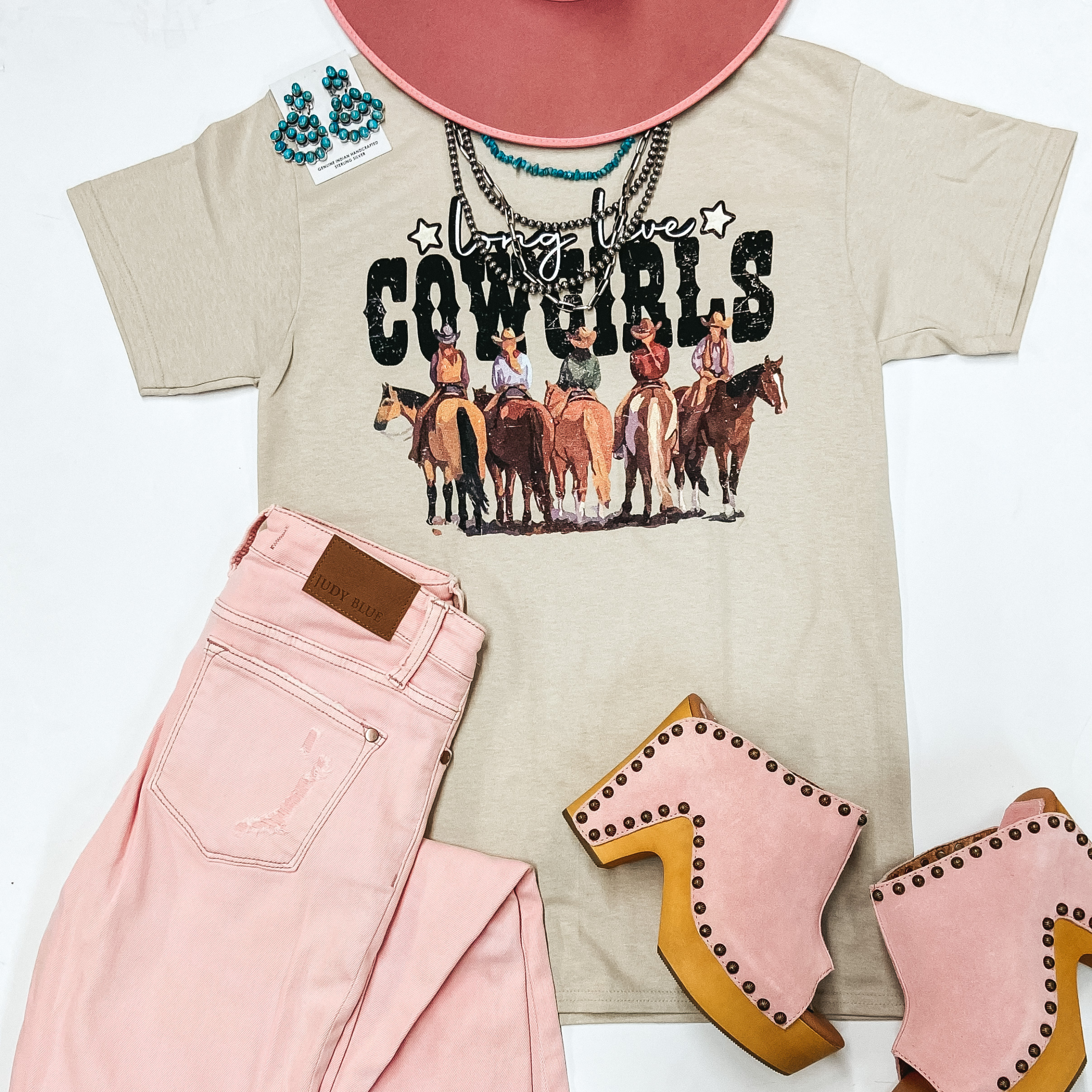 A beige graphic tee with cowgirls on horses that says "Long Live Cowgirls." This tee is pictured on a white background with genuine Navajo Jewelry and pink jeans, pink wedges, and a pink hat.