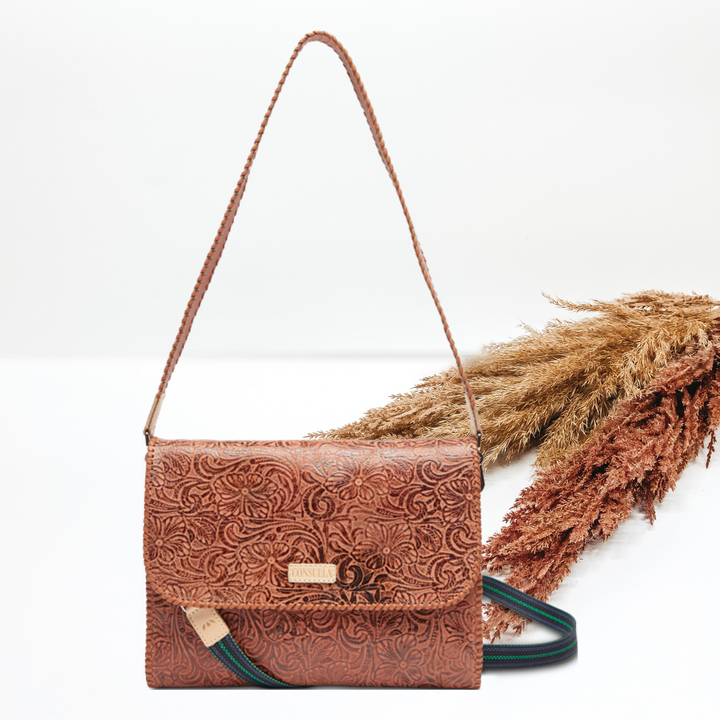 Pictured is a rectangle purse with two different straps. This purse is a tooled leather design. This purse is pictured on a white background with pompous grass on the right side of the picture.