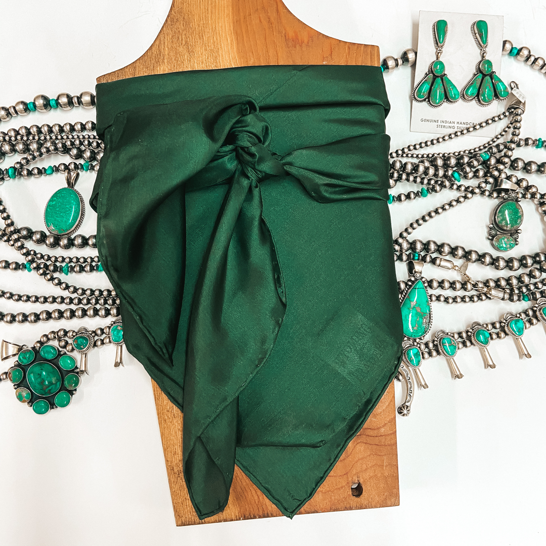 A solid color wild rag tied around a wooden display. Pictured on white background with turquoise jewelry.