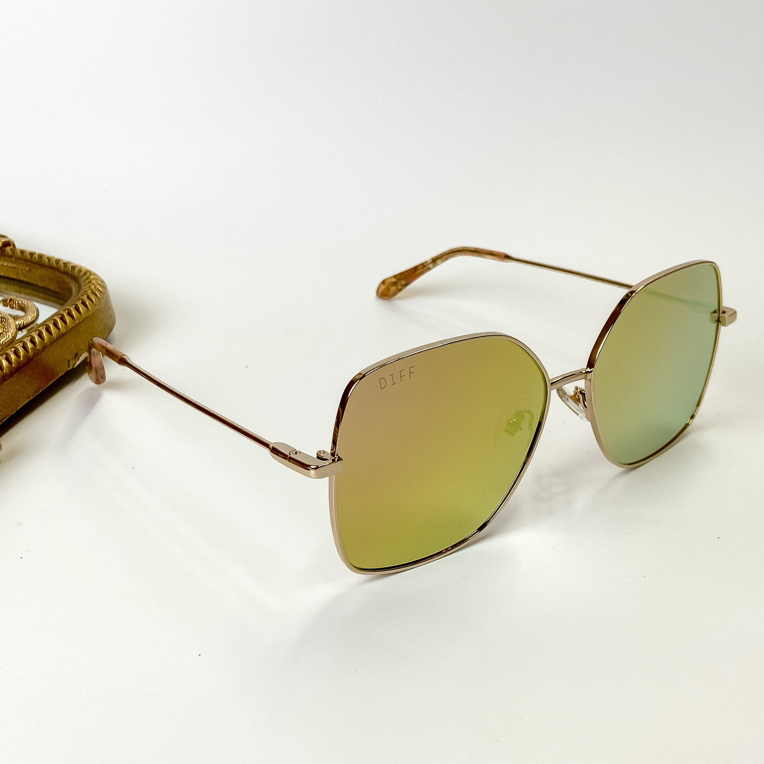 A pair of gold tone frame sunglasses with pink ad yellow mirror lenses. These sunglasses are pictured on a white background with gold jewelry.