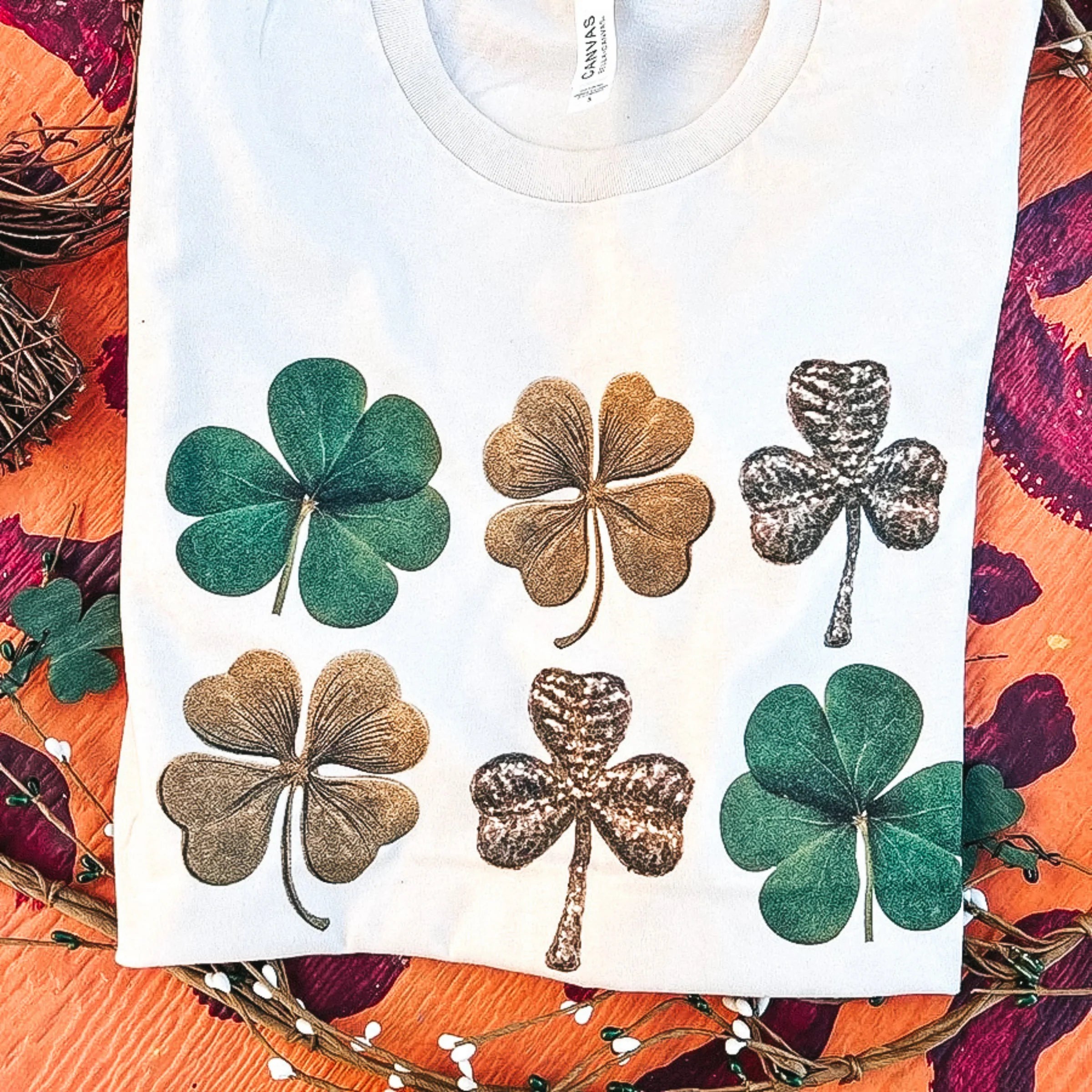 An ivory tee shirt with with a shamrock graphic. Pictured on leopard print background.