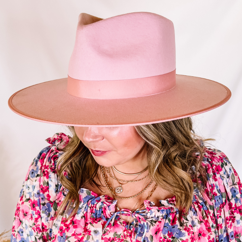Model is wearing a light pink felt hat with a light pink ribbon. Model has it paired with a pink and blue floral top and gold jewelry.