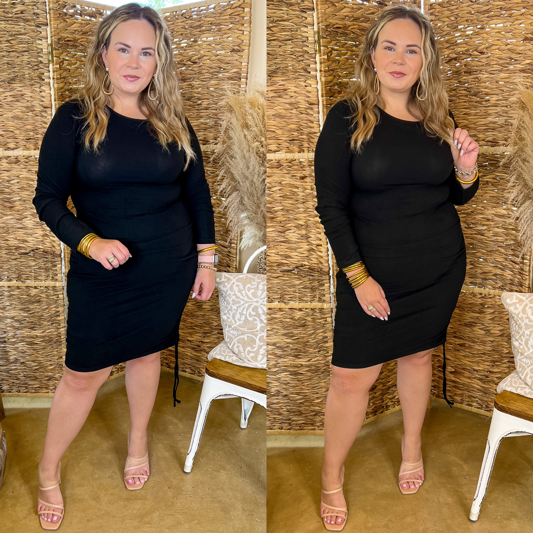Model is wearing a black fitted dress with ruched hips and long sleeves. Model has it paired with nude heels and gold jewelry.