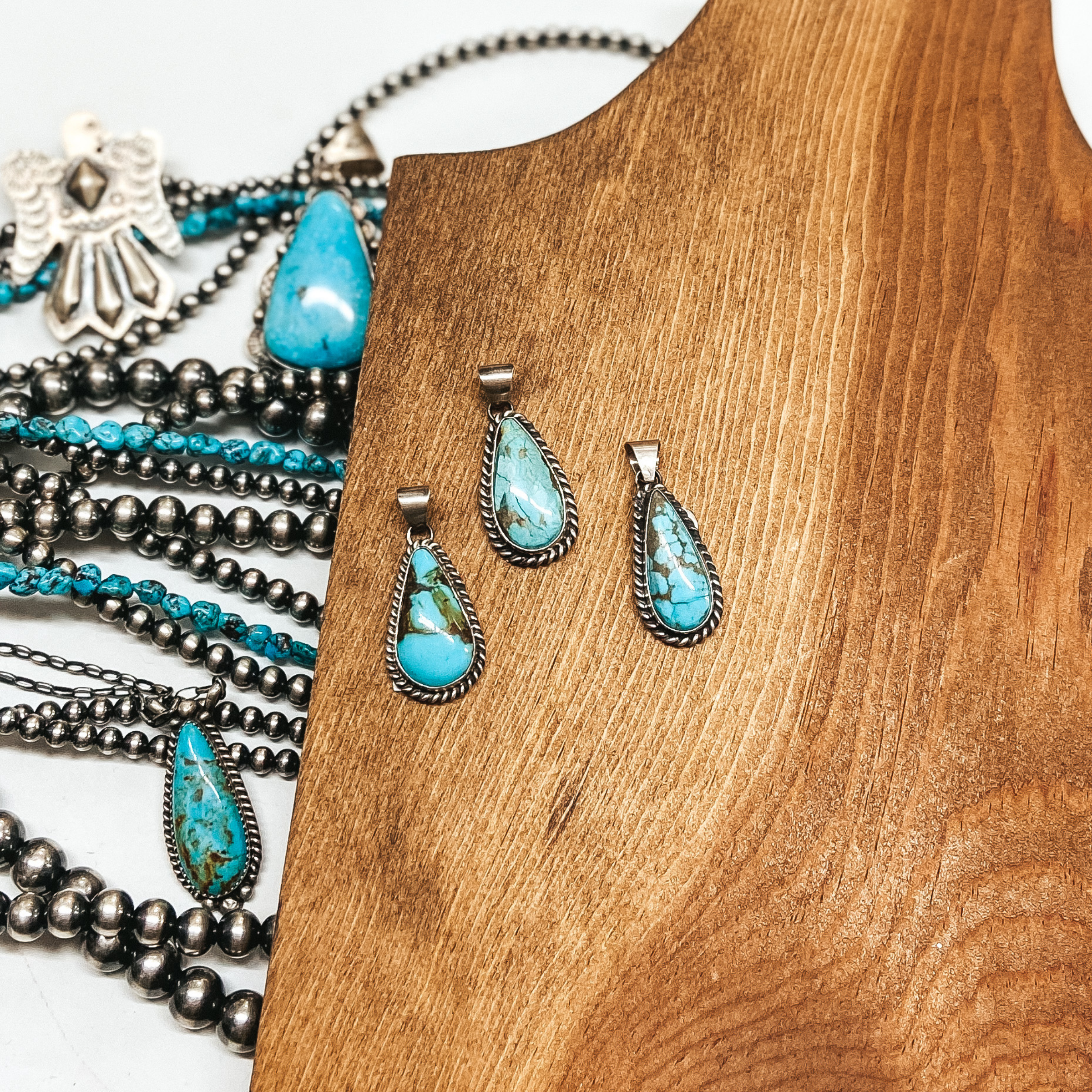 Three turquoise teardrop pendants pictured on wooden background with Navajo pearls and turquoise jewelry.