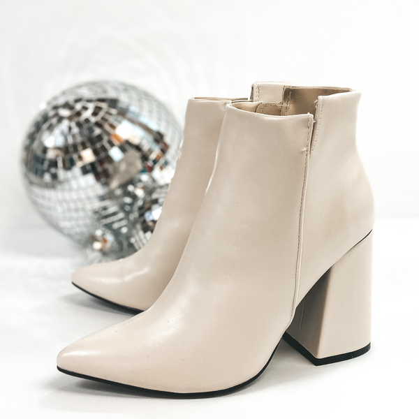 These booties have a high block heel with an asymmetrical ankle. The zip up booties have a pointed toe and are pictured on a white background with disco balls.