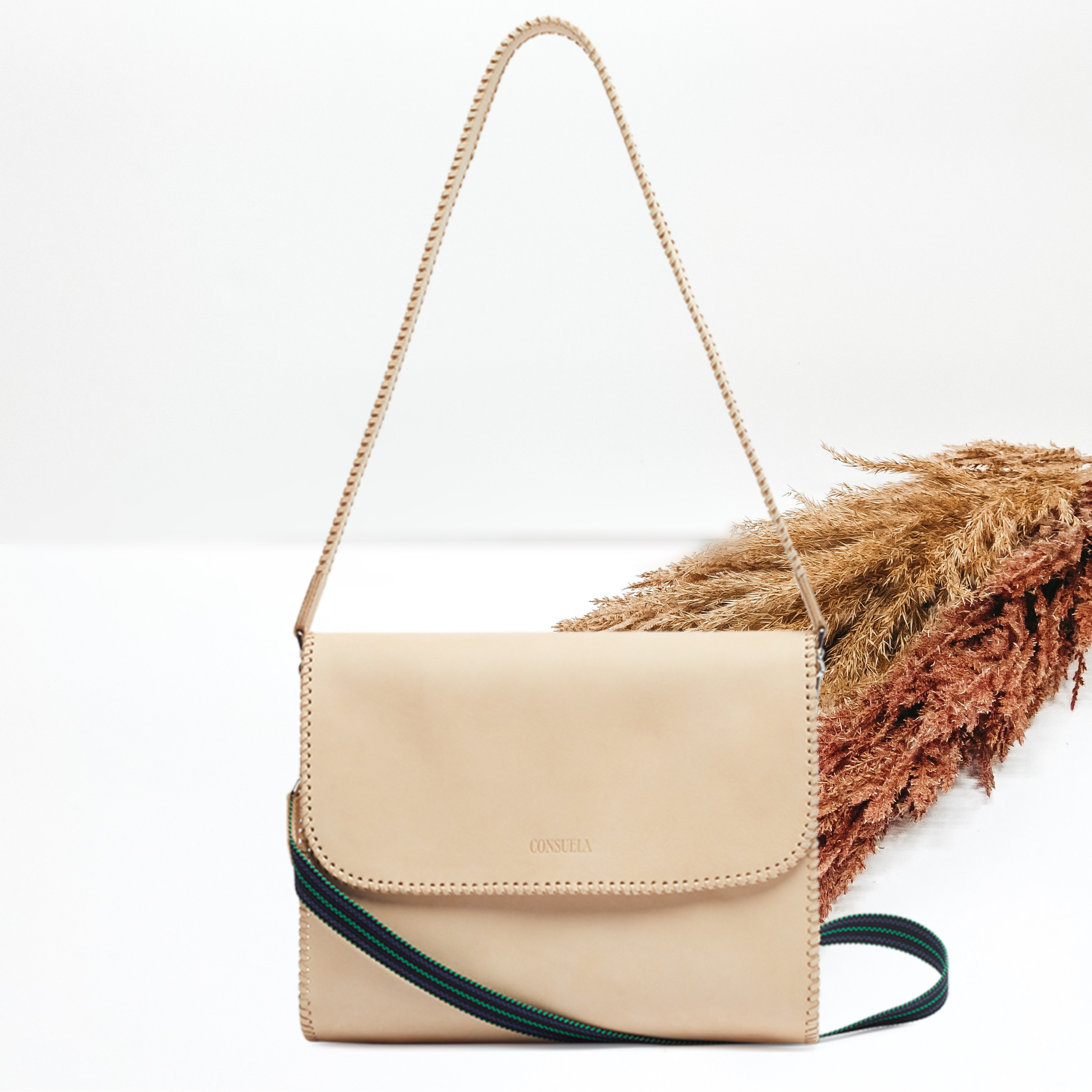 Pictured is a rectangle purse with two different straps. This purse is a light tan leather all over design. This purse is pictured on a white background with pompous grass on the right side of the picture.