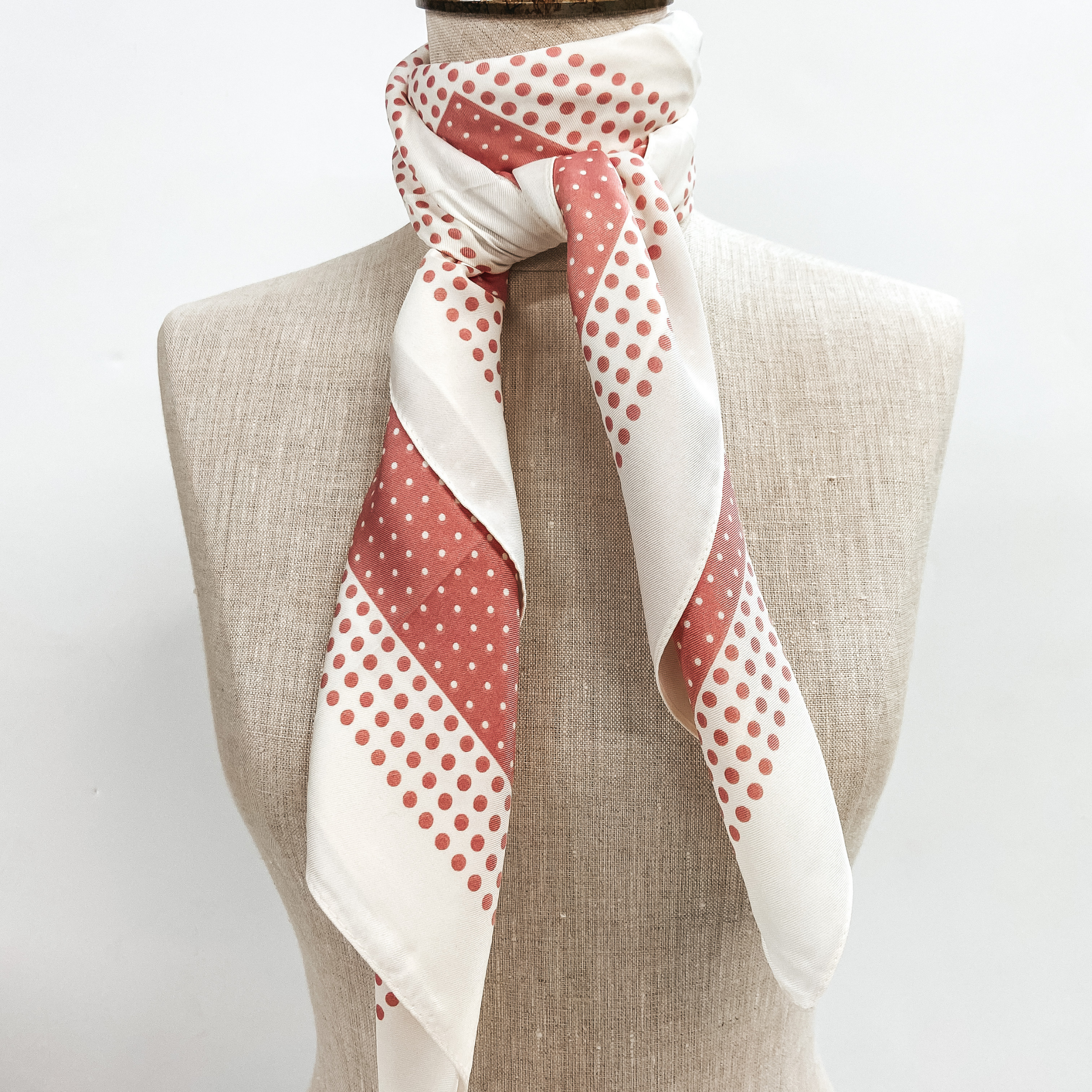 A pink and ivory polka dot scarf tied around the neck of a mannequin. Pictured on white background.