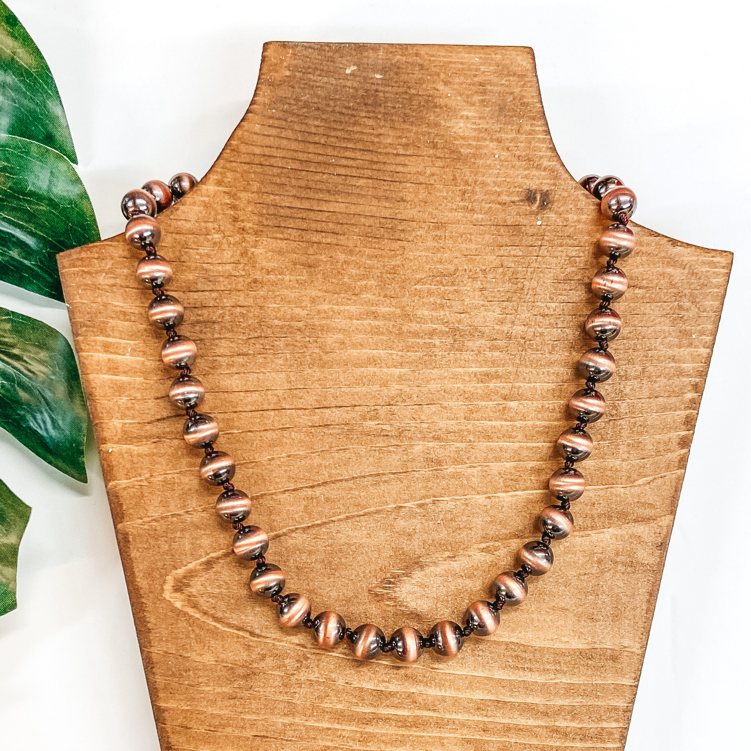 A copper faux Navajo Pearl necklace pictured on a white background with a palm leaf.